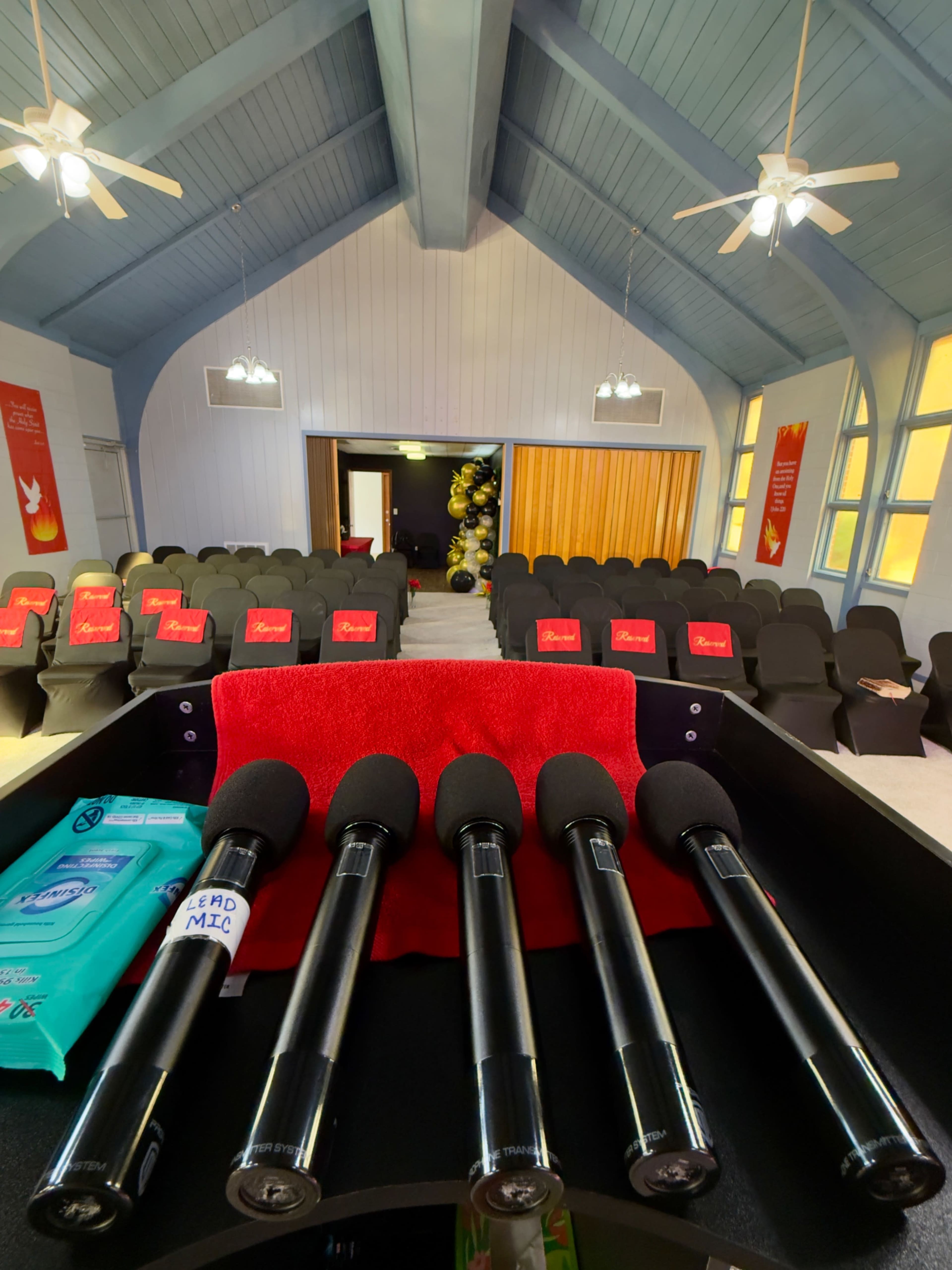 The image shows a microphone setup on a table in a room arranged with rows of black chairs and decorated with banners.