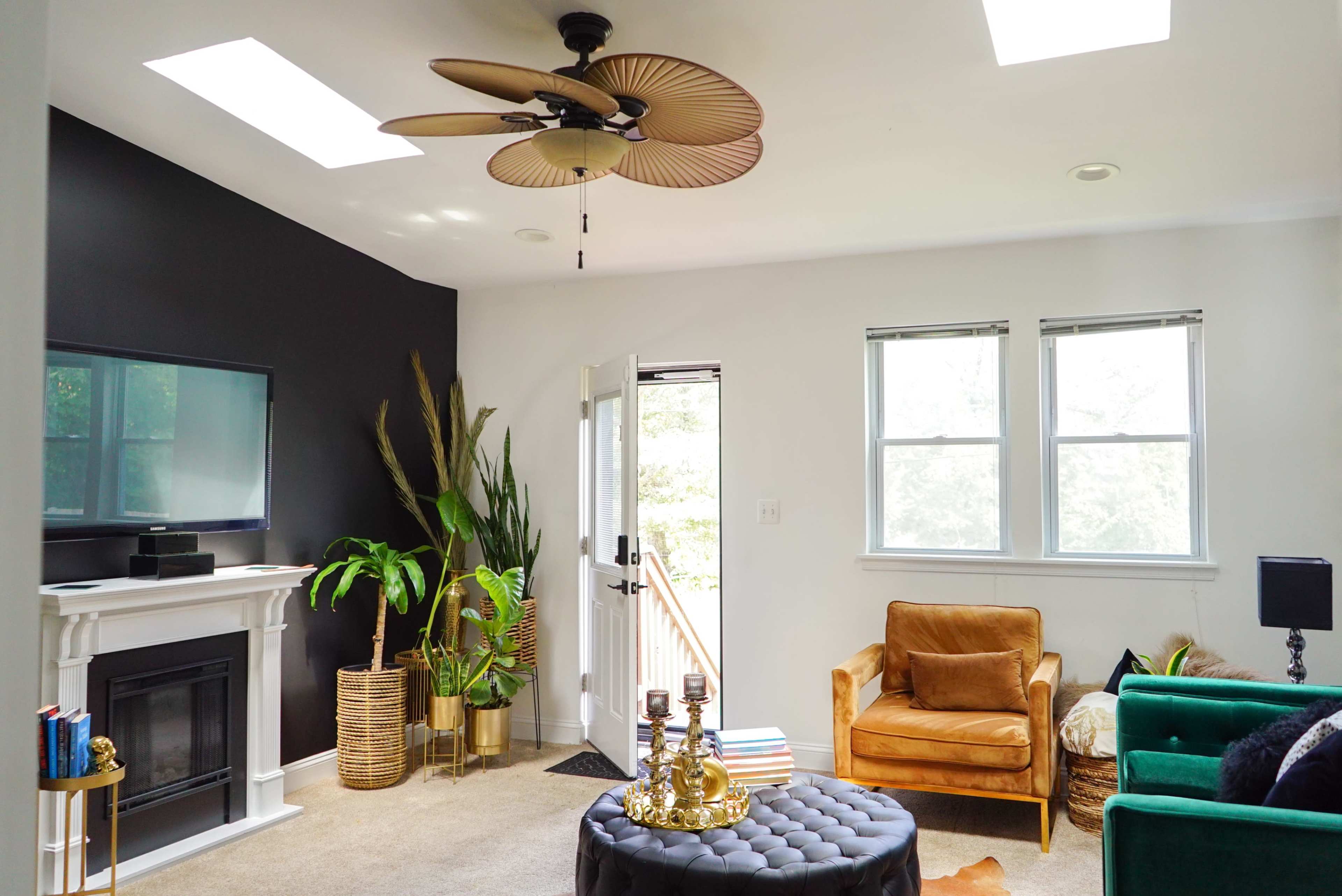 A modern living room featuring a ceiling fan, two windows, a fireplace, and a mix of green and brown furniture.