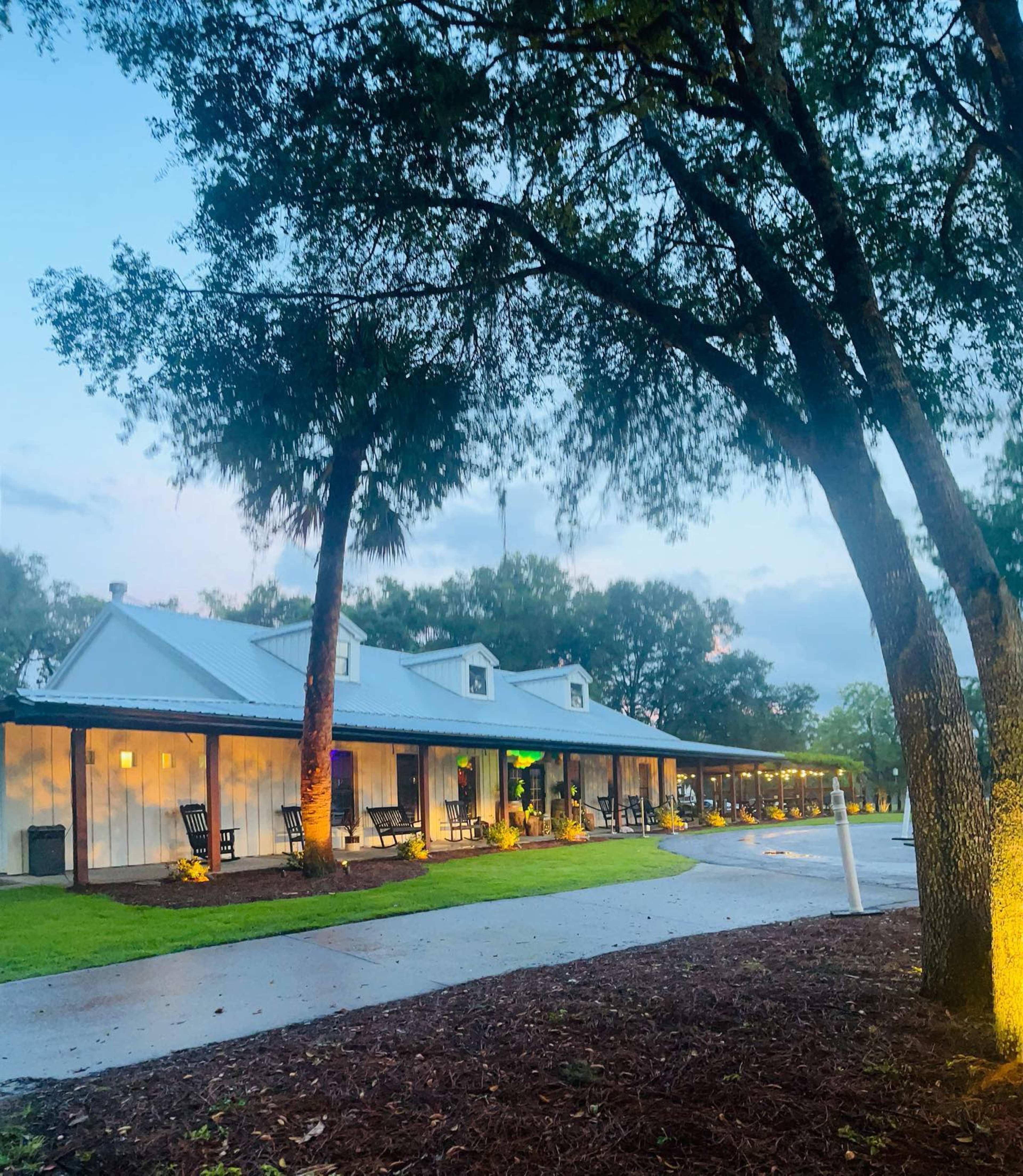 A row of rustic-style buildings with a metal roof is lined along a pathway, surrounded by trees and soft outdoor lighting.