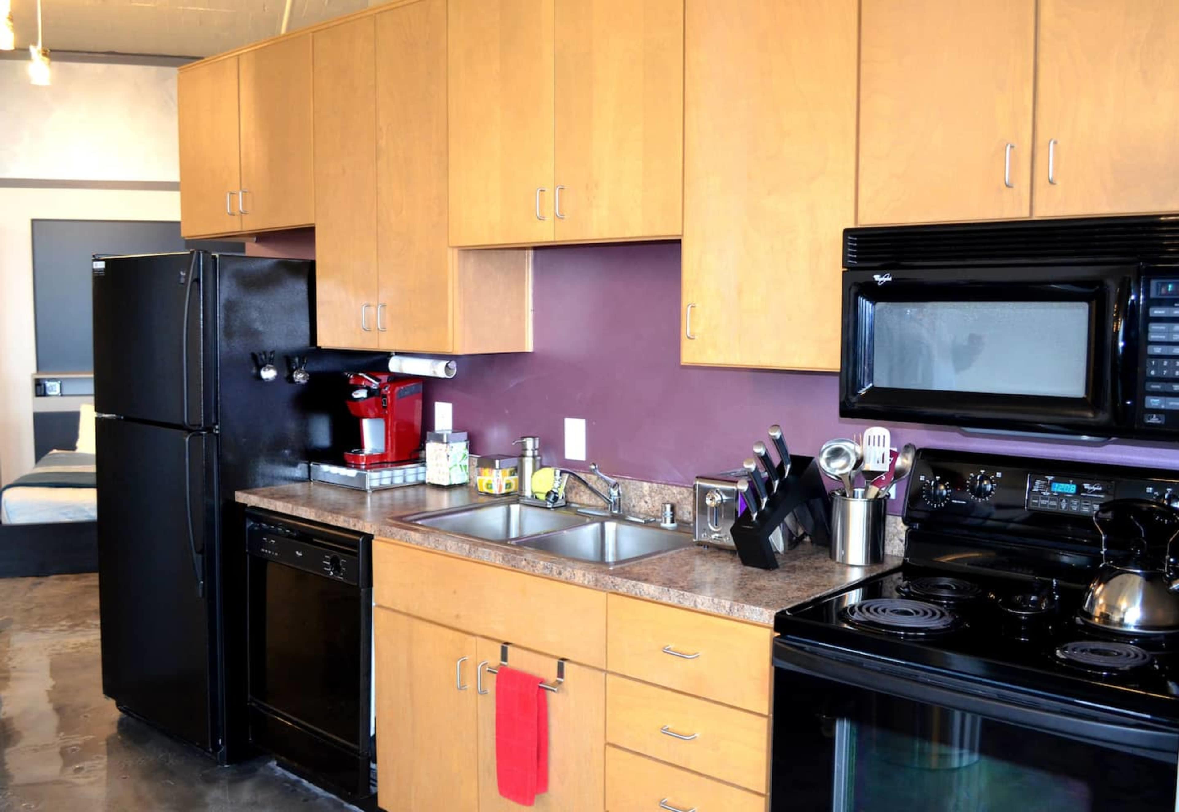 A compact kitchen with wooden cabinets, stainless steel appliances, and a black refrigerator and stove.