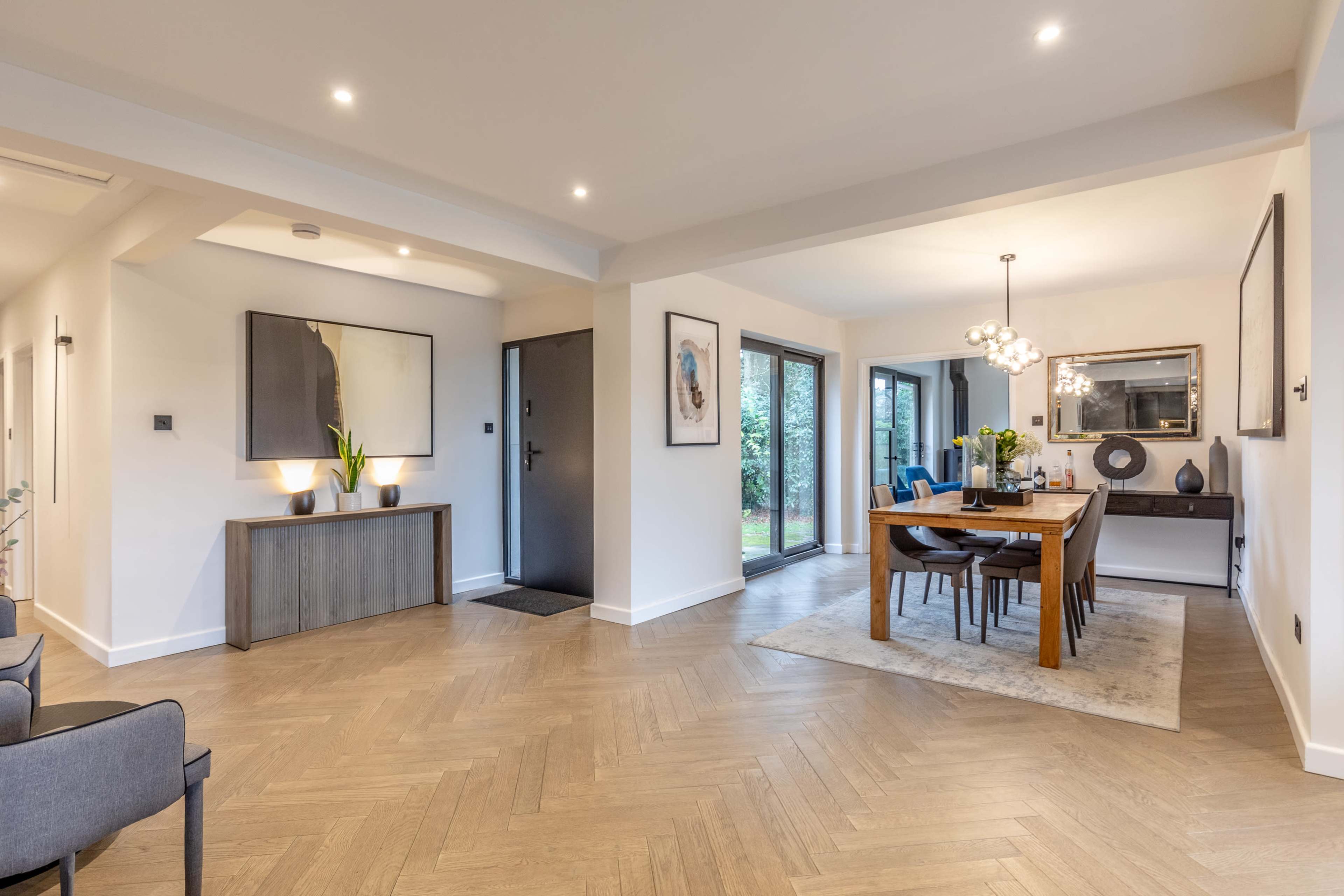 The image shows a modern interior space featuring a dining area with a wooden table, surrounded by chairs, and an entryway with a console table and decorative items.