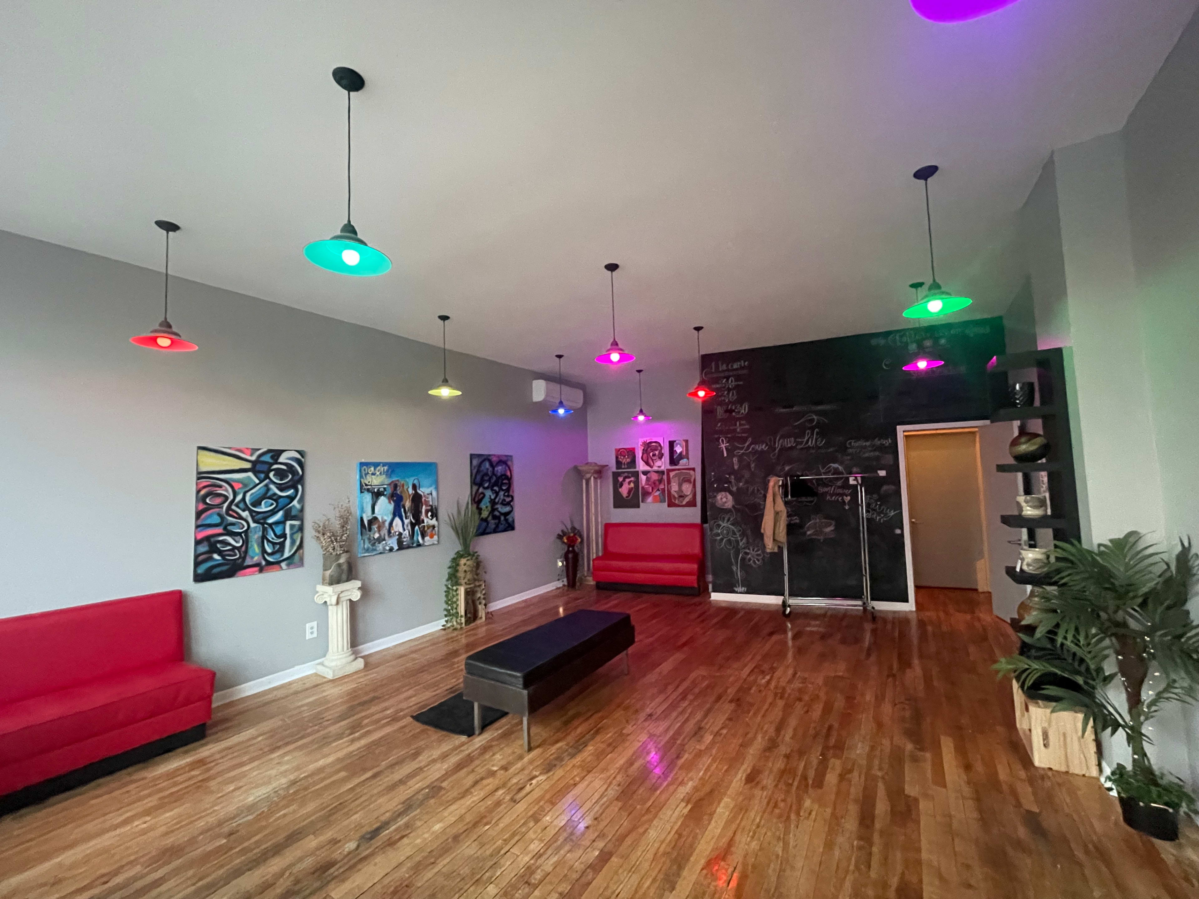 The room features red couches, a dark wall with colorful artwork, and vibrant pendant lights illuminating the space.
