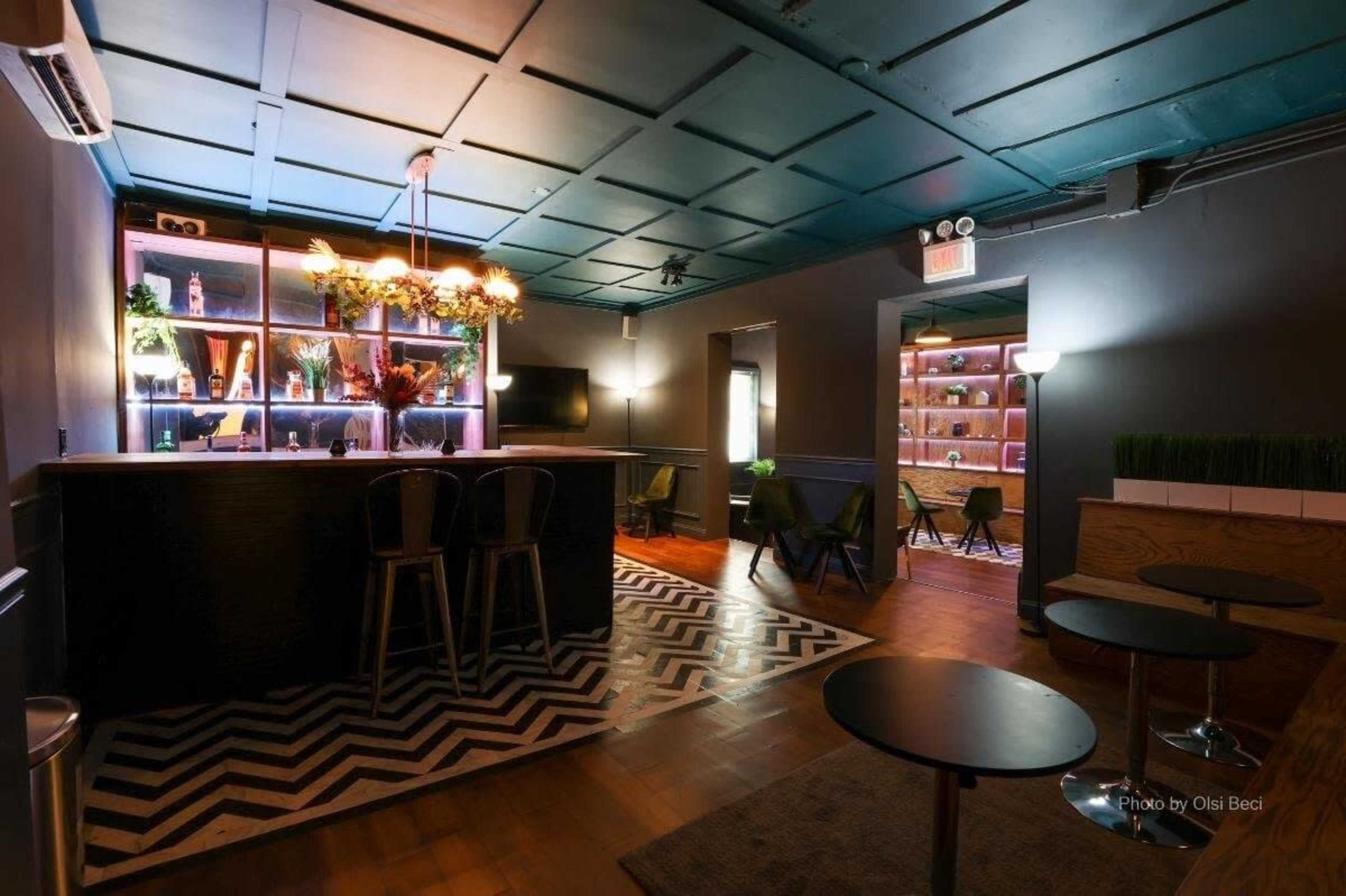 The image shows a modern lounge area with a bar, seating, and decorative lighting elements in a dimly lit space.