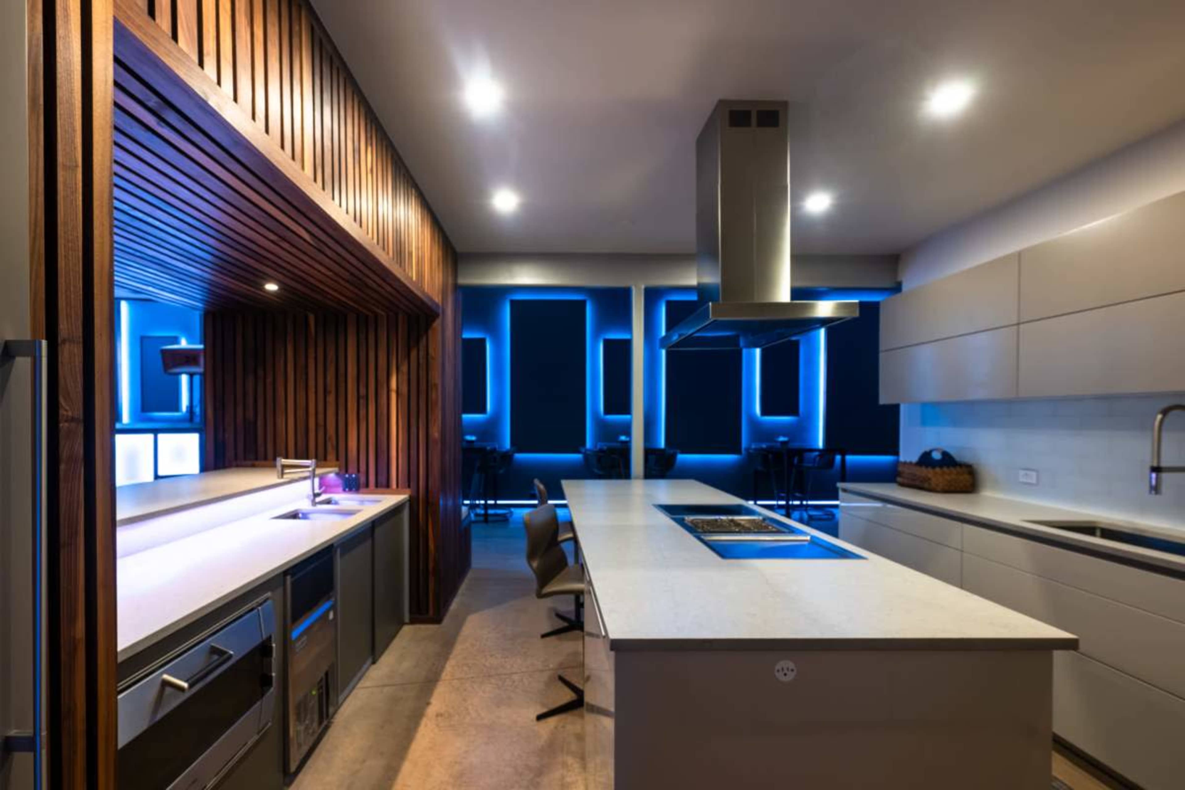 The image shows a modern kitchen with sleek cabinetry, an island with a cooktop, and ambient lighting.