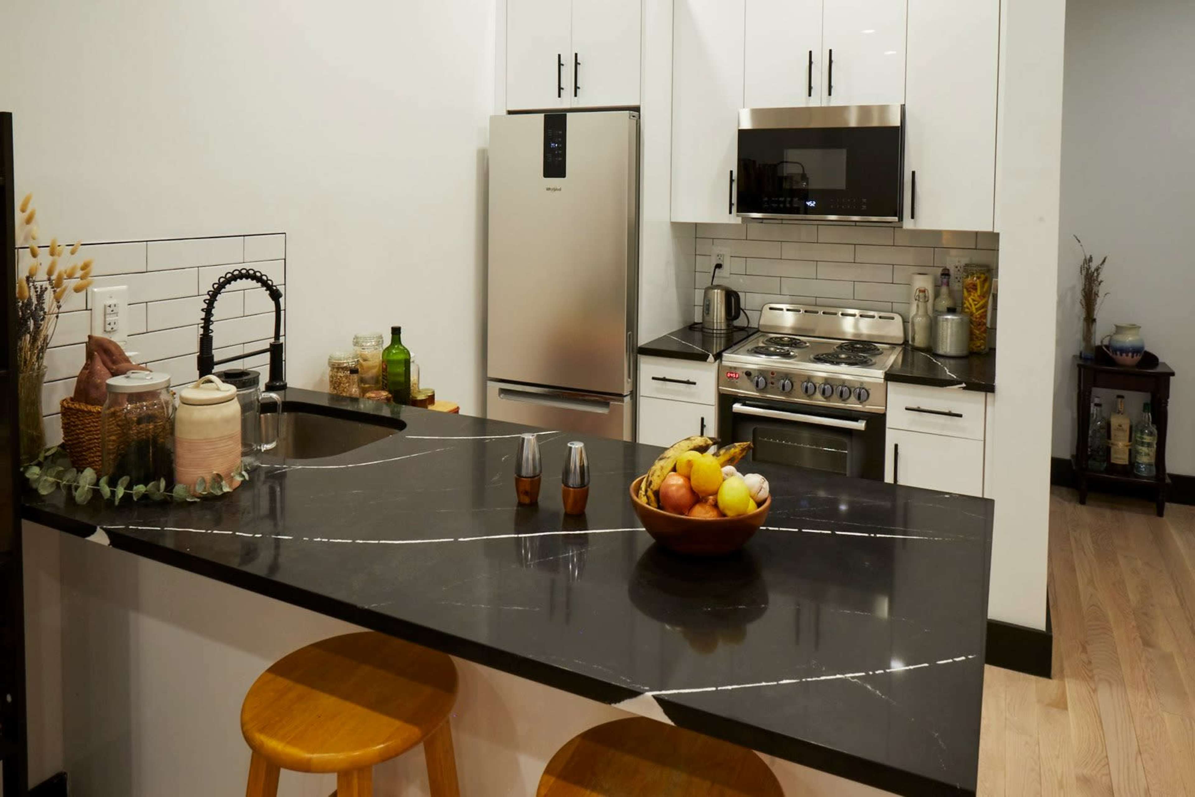 A modern kitchen with black countertops, stainless steel appliances, and a bowl of fruit on the island.