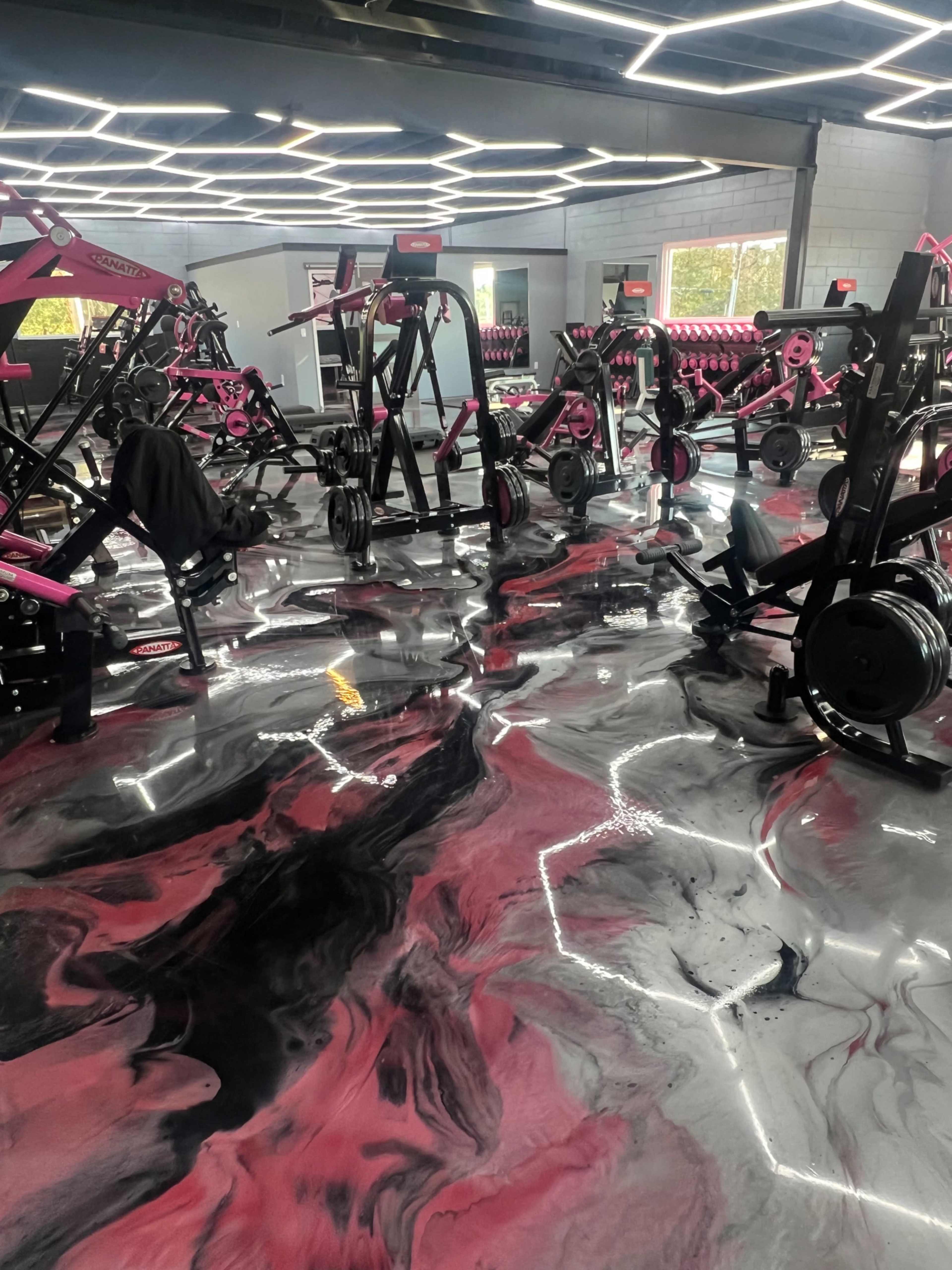 The image shows a gym interior with exercise equipment arranged around a black and pink marbled floor.