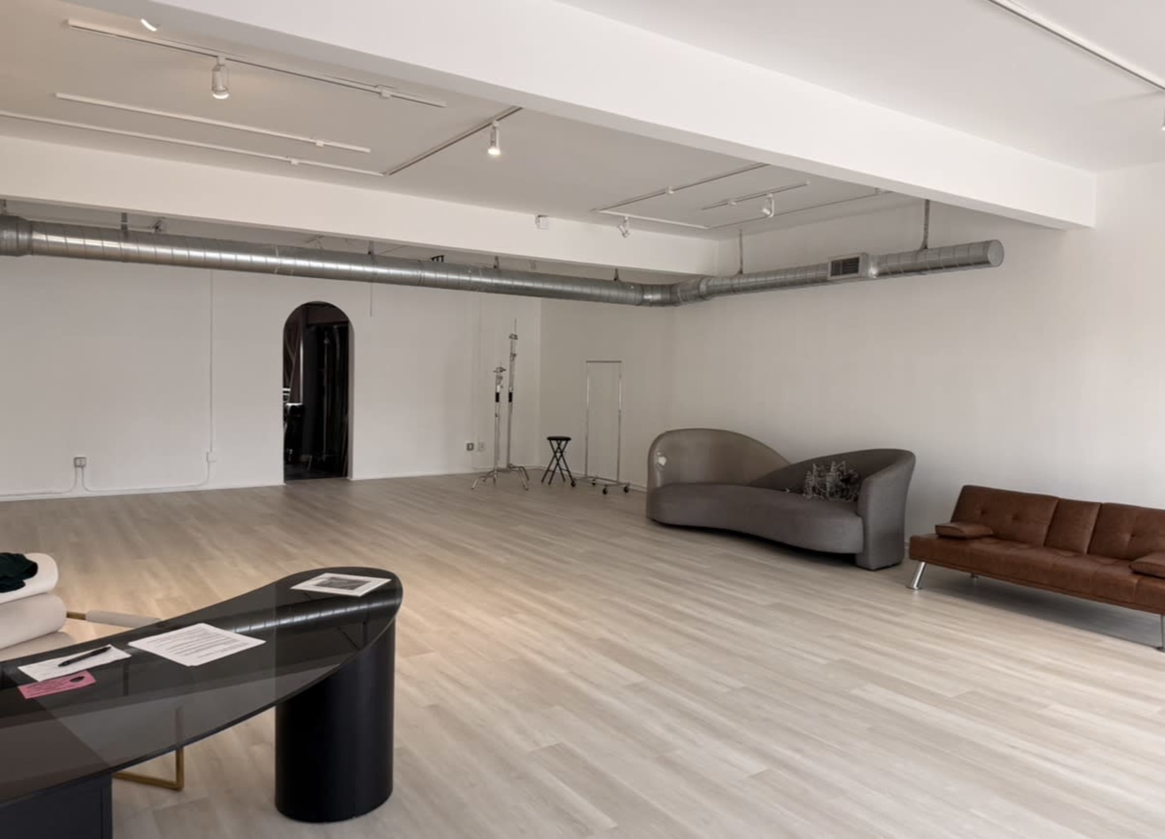 The image shows a spacious, modern interior with light-colored flooring and minimal furniture, including a brown sofa and a curved gray seating area.