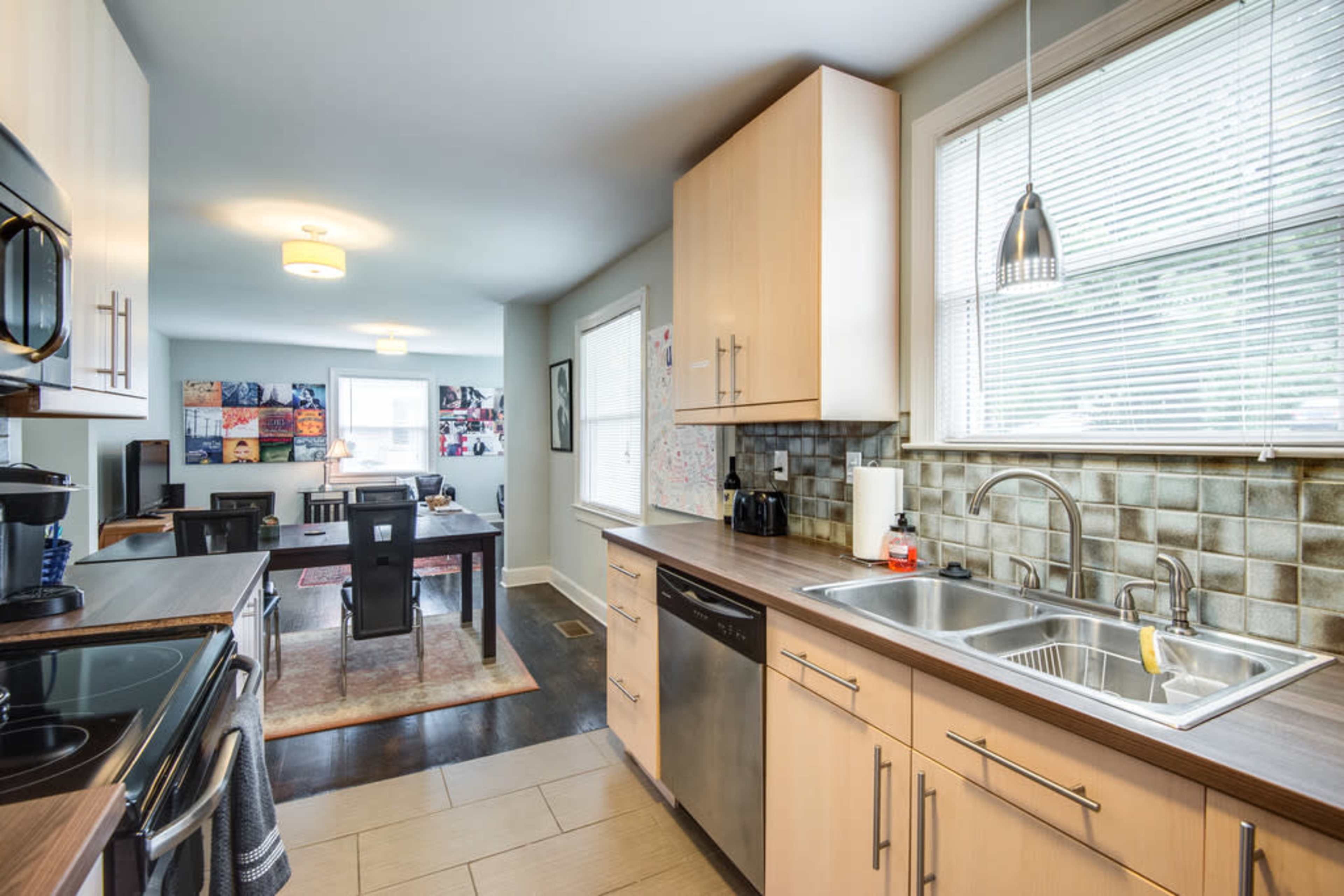 A modern kitchen features wooden cabinets, stainless steel appliances, and a double sink, with an open layout leading into a dining area visible in the background.