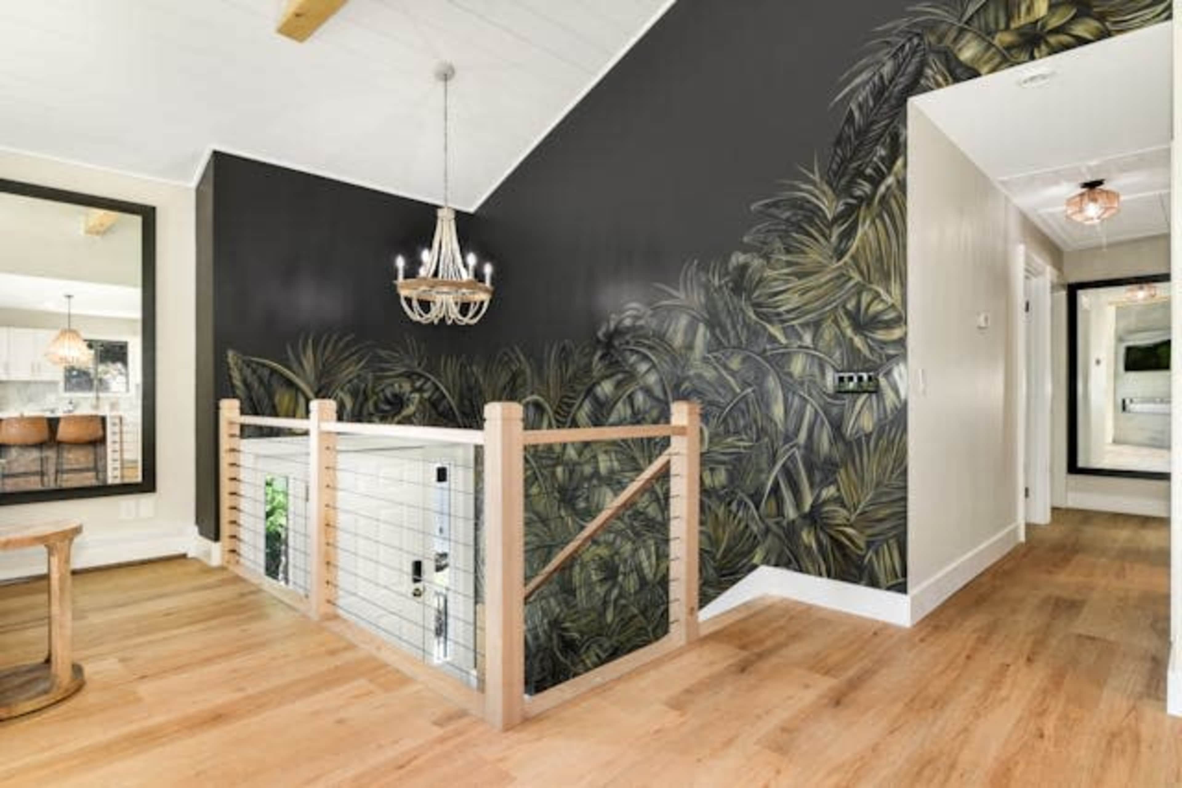 The image shows a modern interior space featuring a staircase with a wooden railing and a large mural of tropical plants on one wall.
