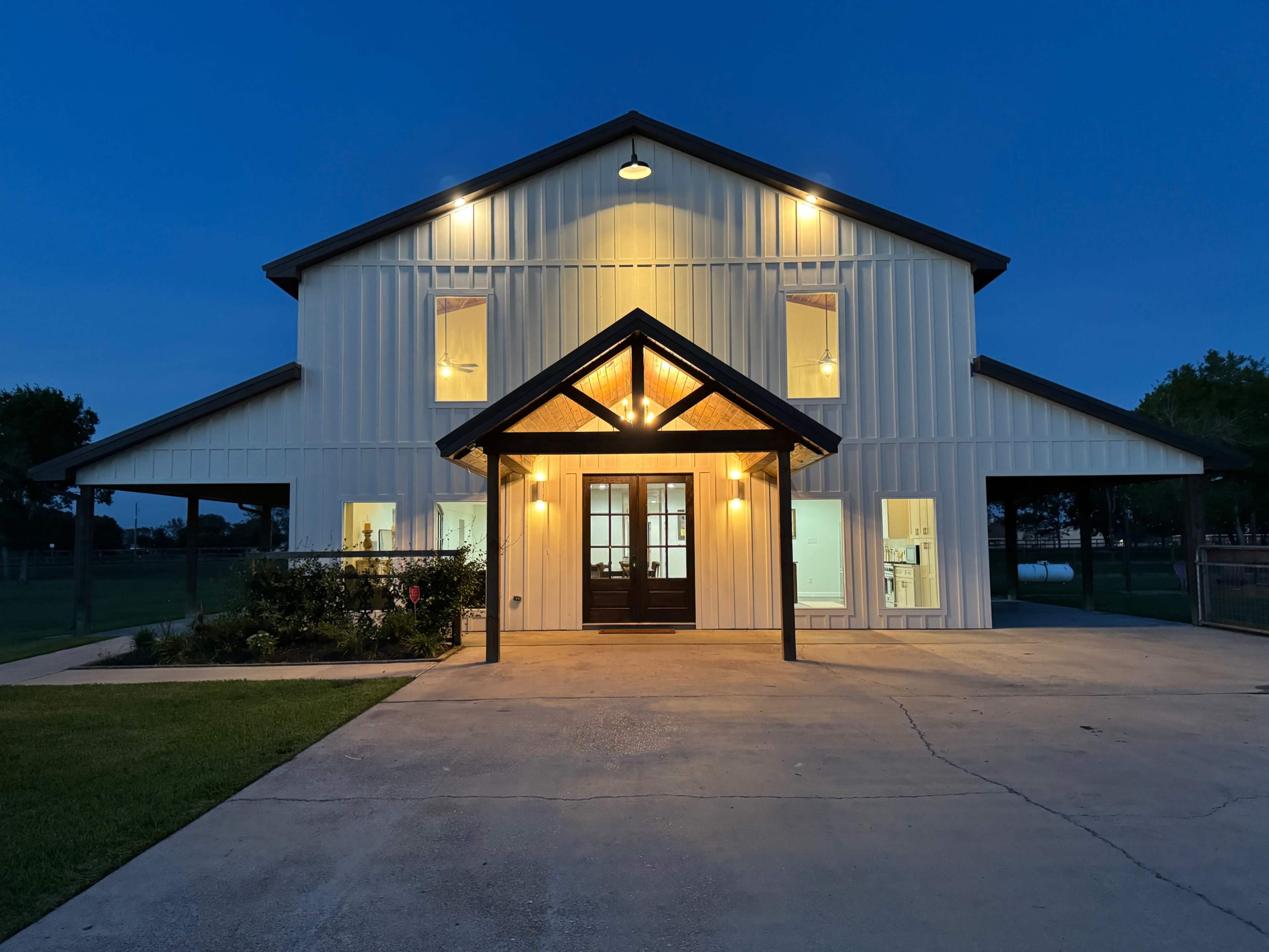 A modern farmhouse-style building is illuminated at night, featuring a gabled roof, large windows, and a front porch.