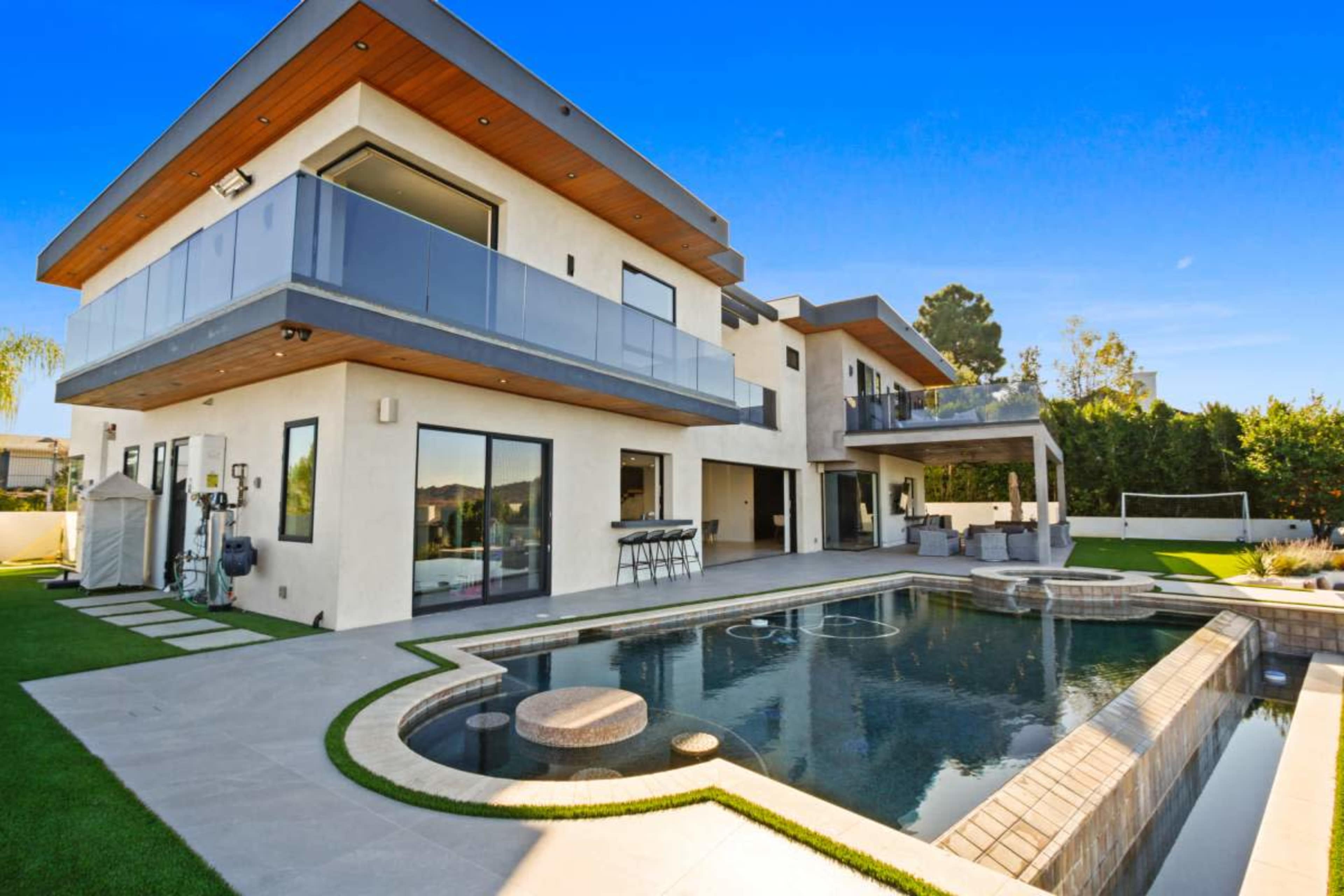 The image depicts a modern two-story house with large windows, a swimming pool, and a green lawn.