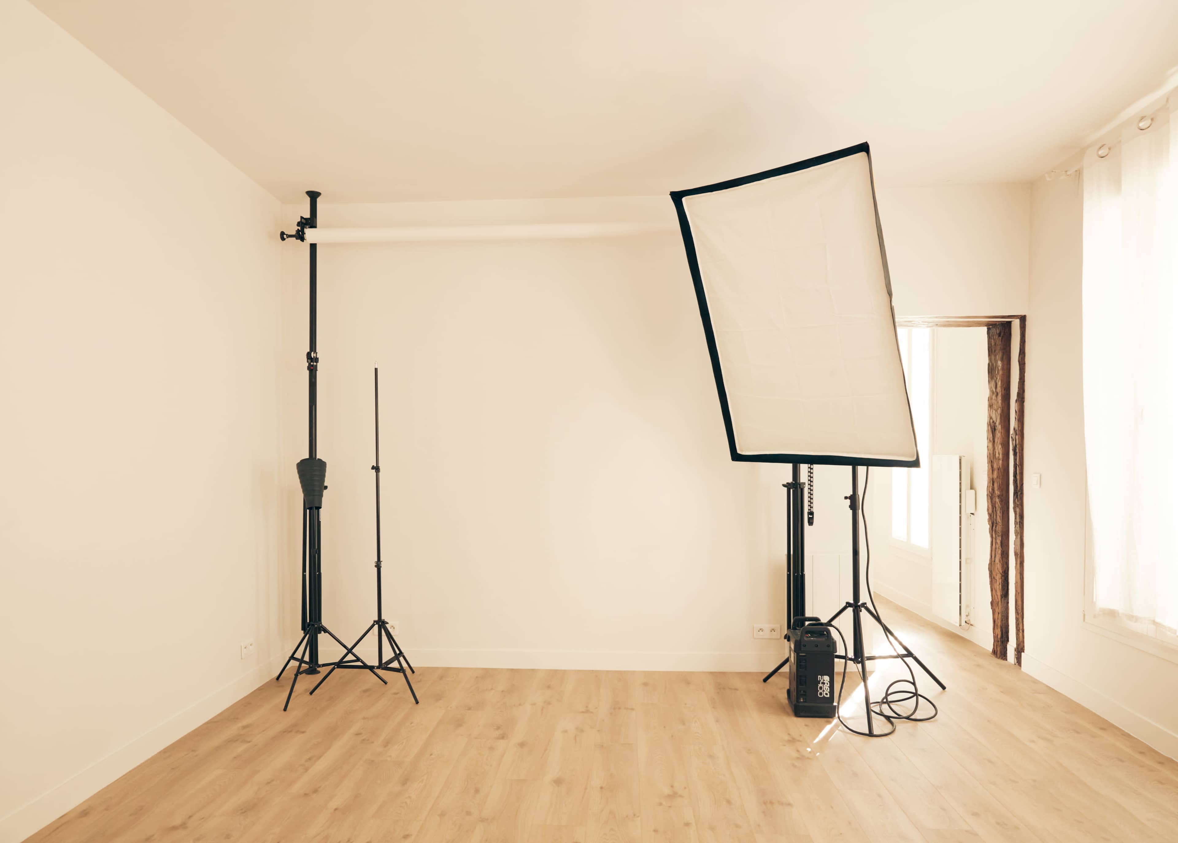 A minimalistic studio space featuring two light stands and a large softbox against a plain wall.