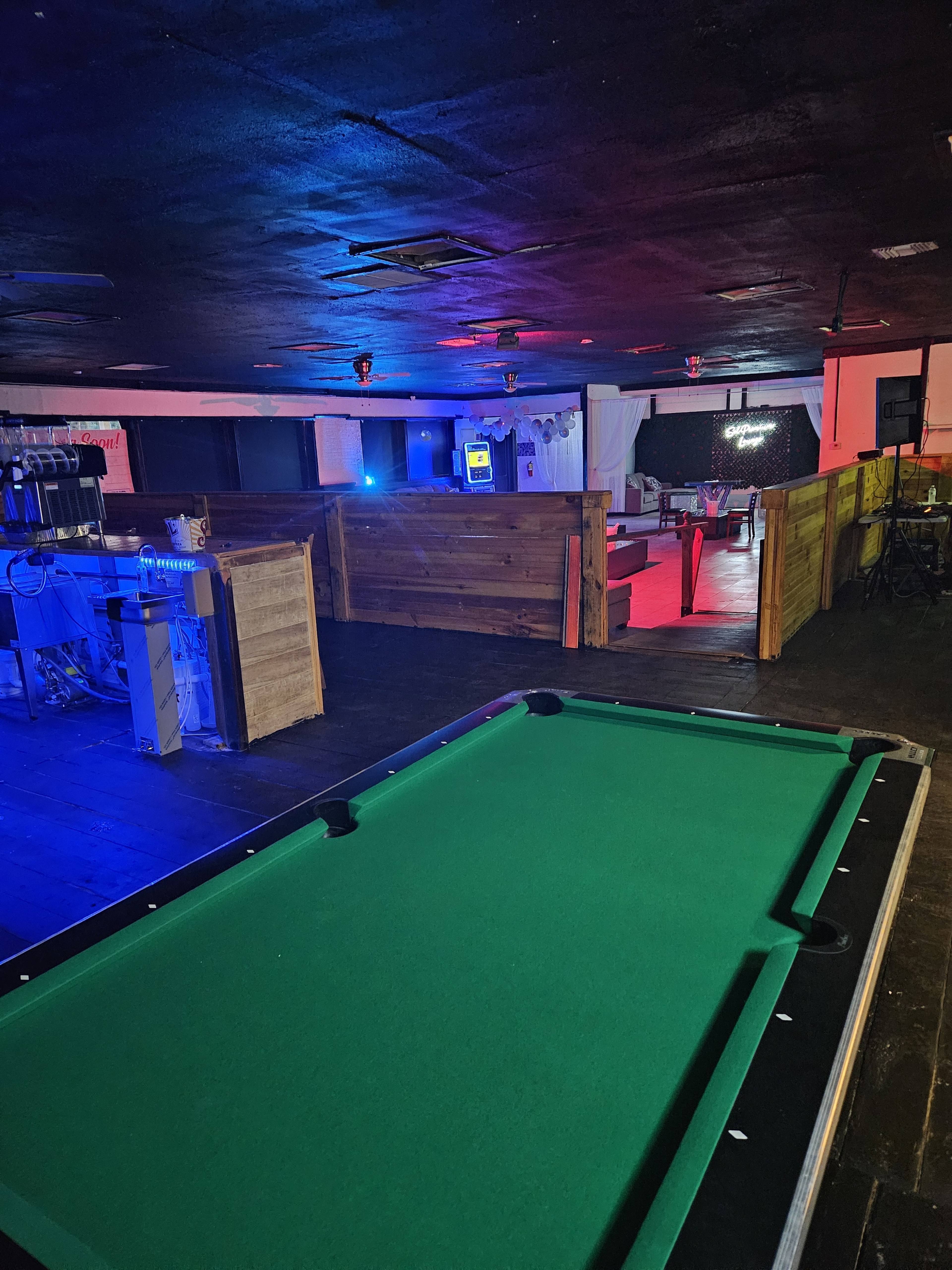 An interior space featuring a green pool table, wooden partitions, and dim lighting with colorful accents.