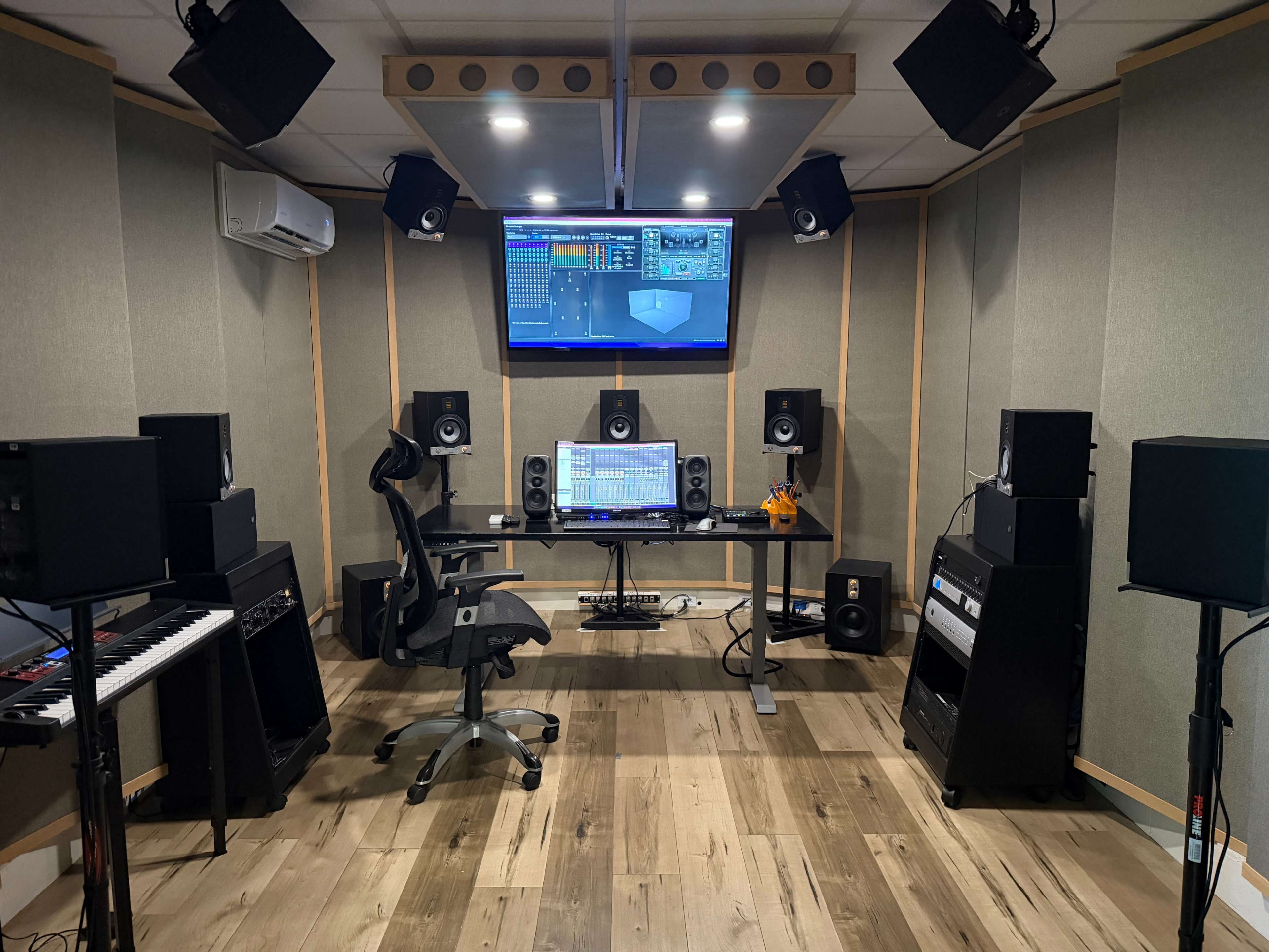 The image shows a recording studio featuring a digital audio workstation, multiple speakers, a keyboard, and soundproof walls.