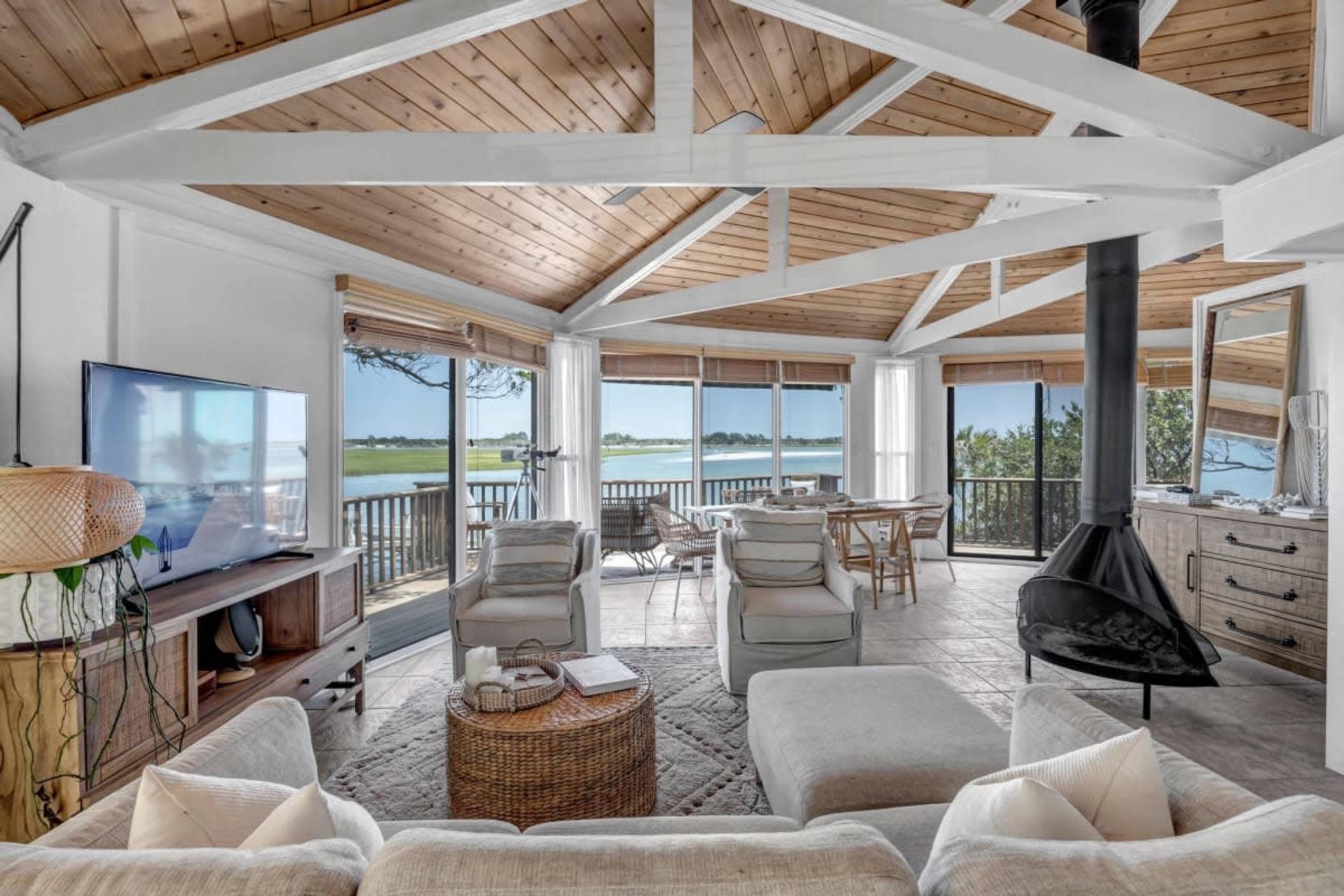 A spacious, open living area features a large window overlooking a body of water, modern furniture, and a black fireplace.