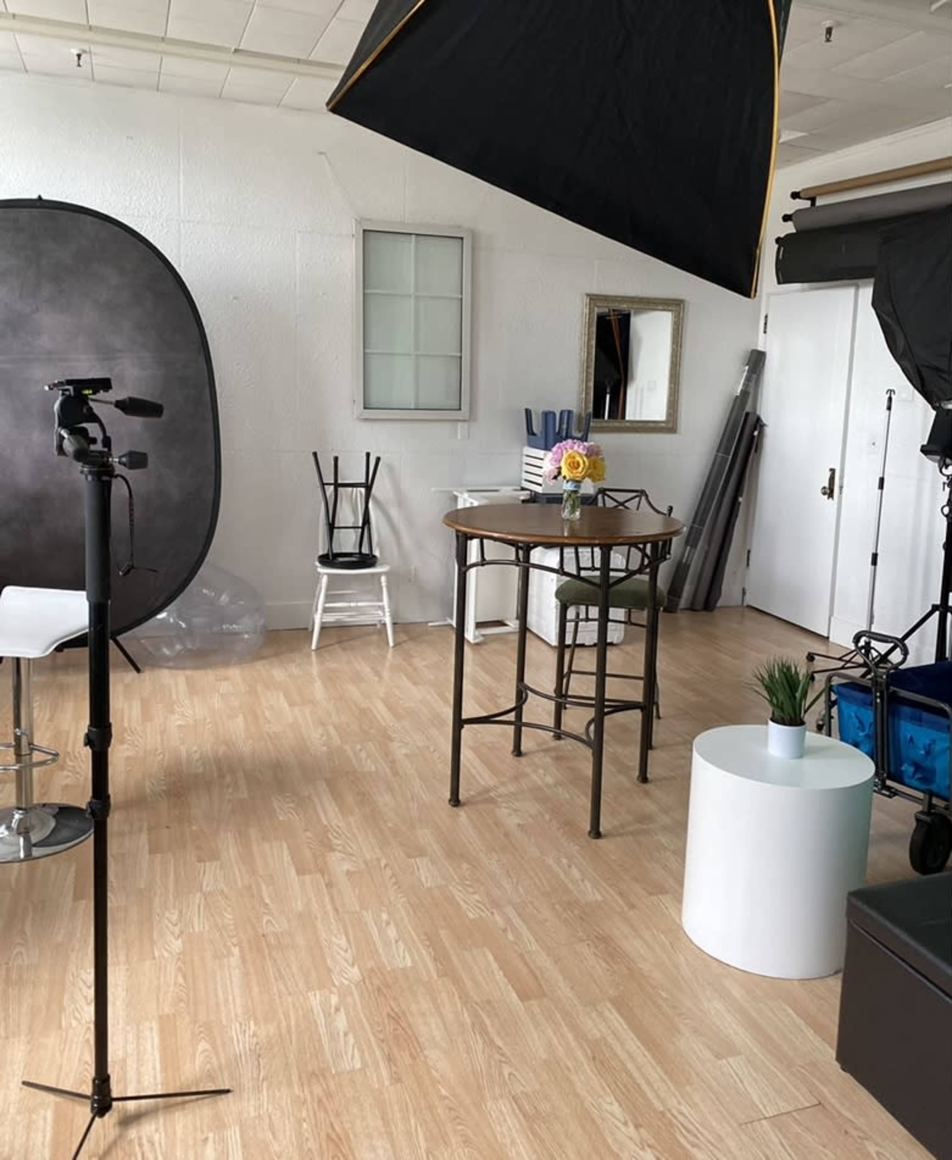 A photography studio with various equipment, a small round table with a flower vase, and a couple of chairs.