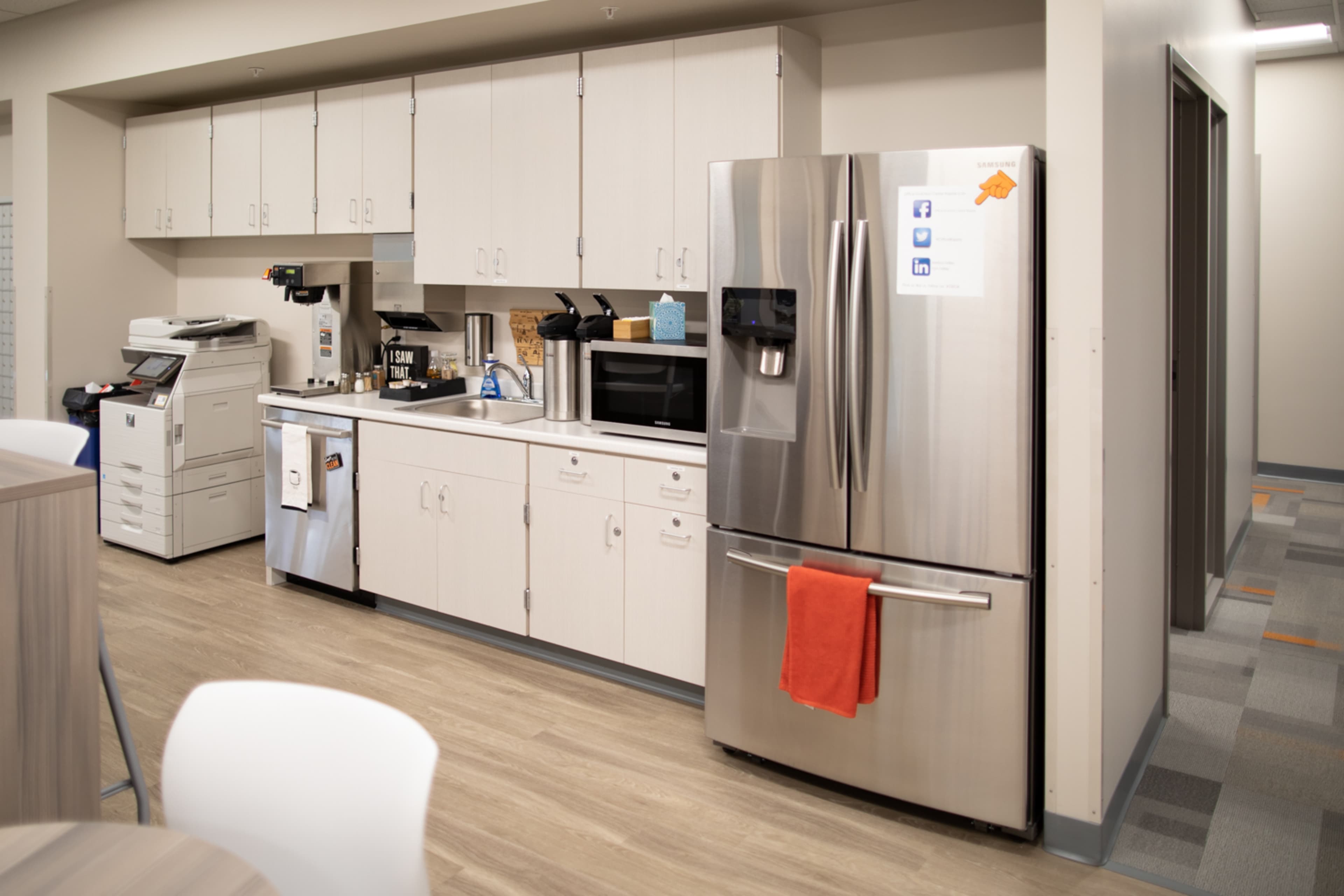 A modern kitchen area with cabinetry, a refrigerator, a microwave, and coffee-making equipment.