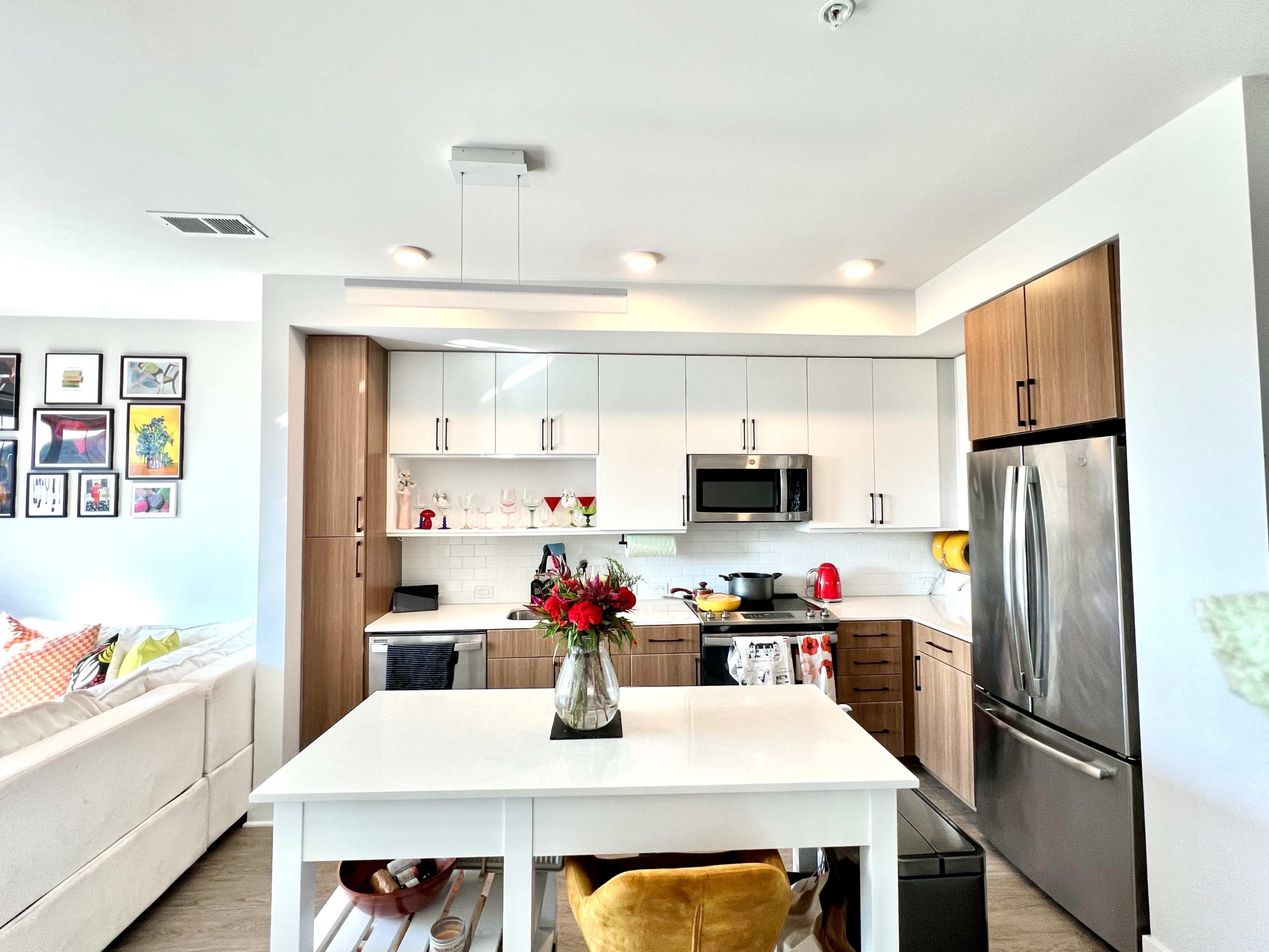 A modern kitchen features white cabinets, stainless steel appliances, and a central island with a vase of flowers.