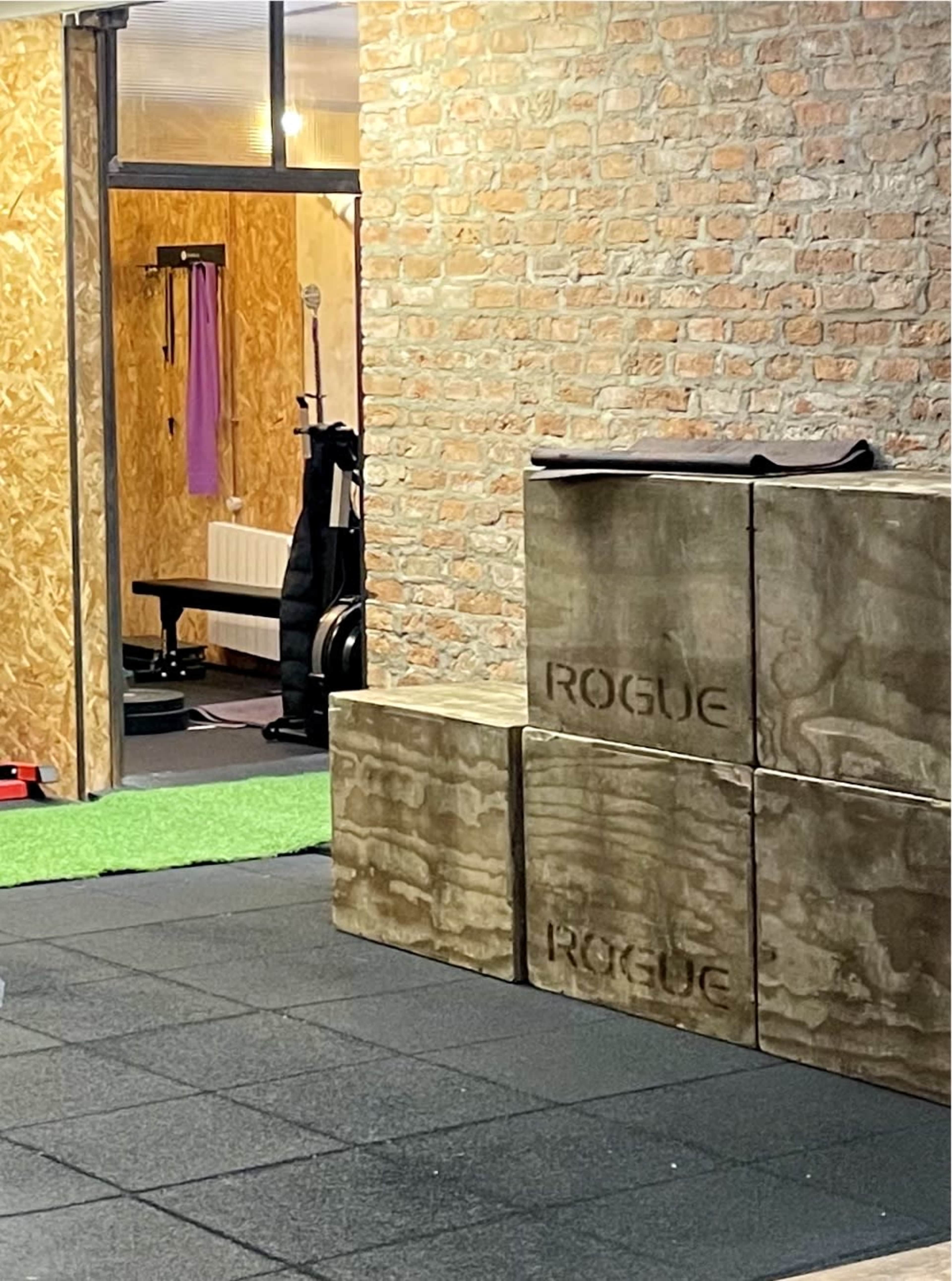 A workout space with concrete blocks labeled "ROGUE," a green turf area, and a wooden wall.