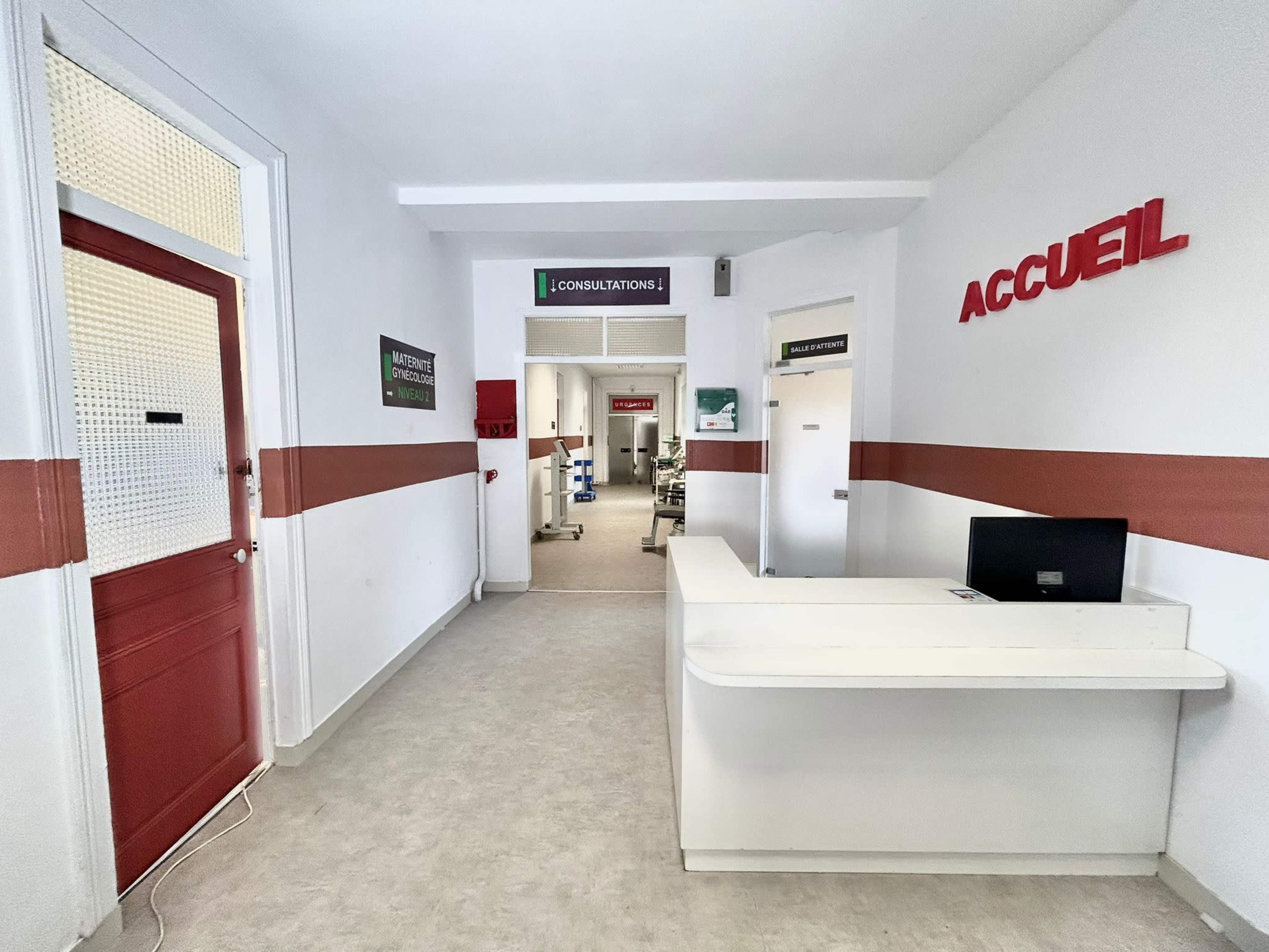 A well-lit hospital corridor featuring a reception desk and signs indicating consultations and patient reception areas.