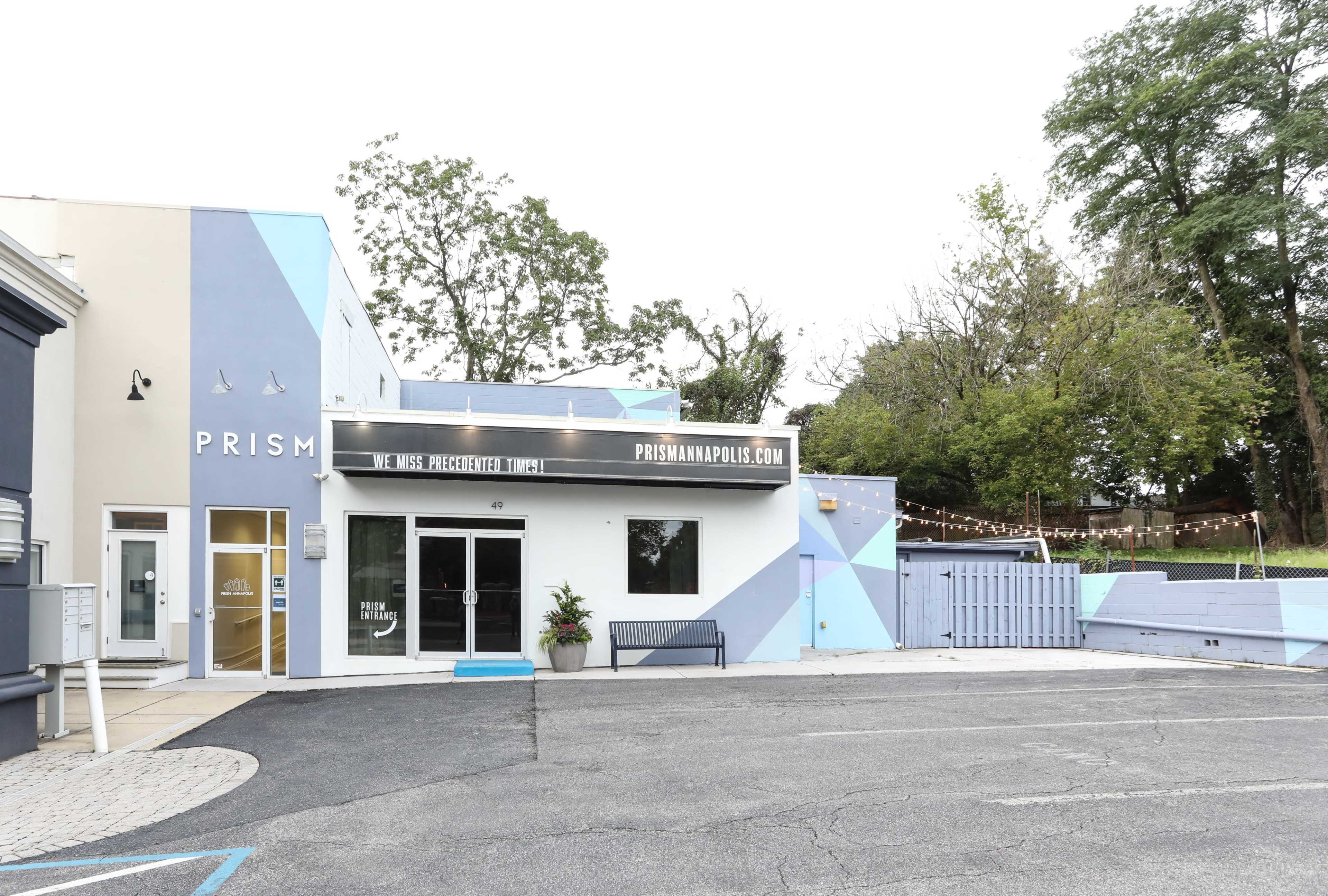 A modern building with a geometric blue and gray mural, featuring signage for "PRISM" and a well-maintained parking area in front.