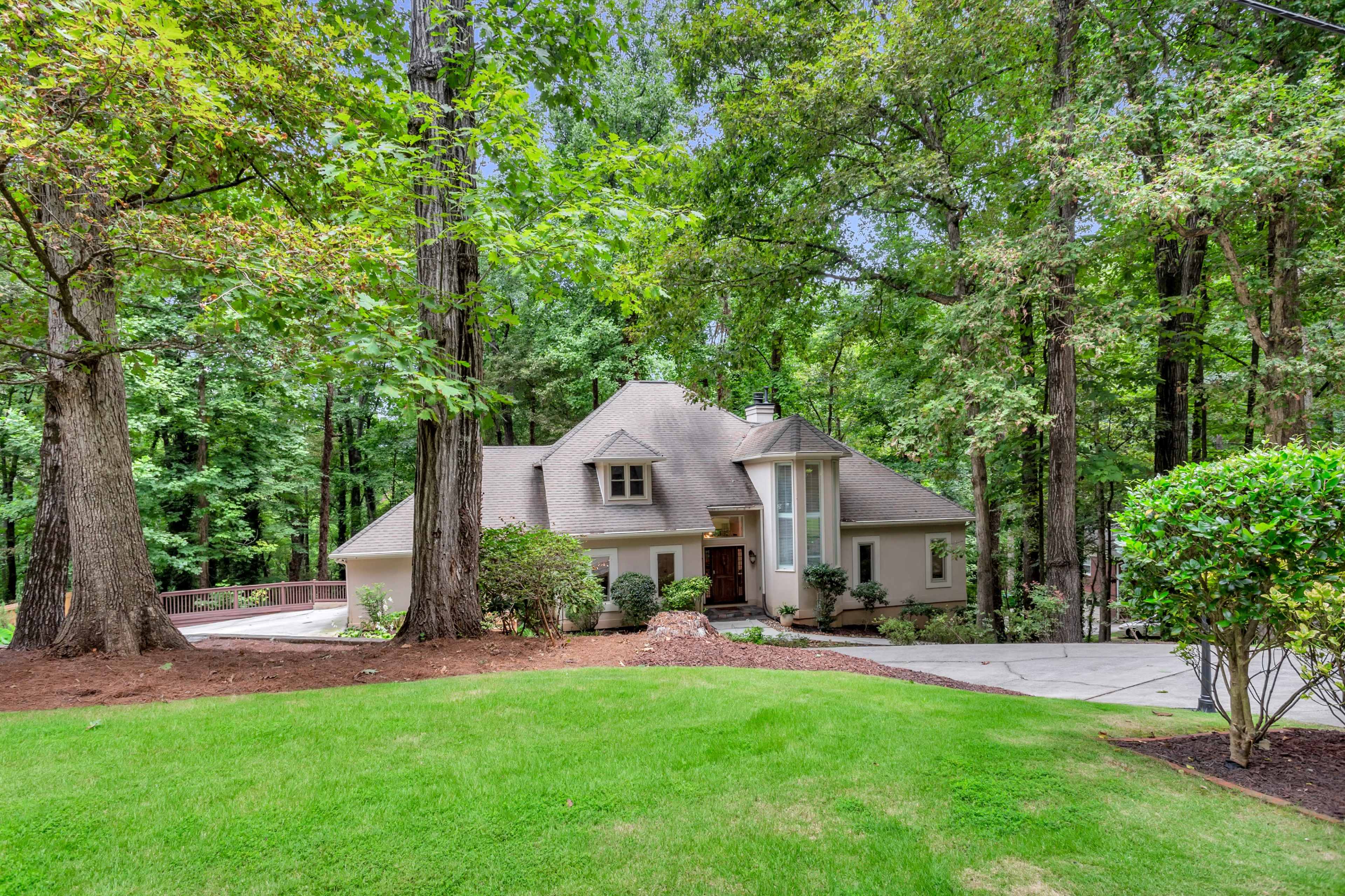 A modern house with a sloped roof is situated amid tall trees and a well-maintained lawn.