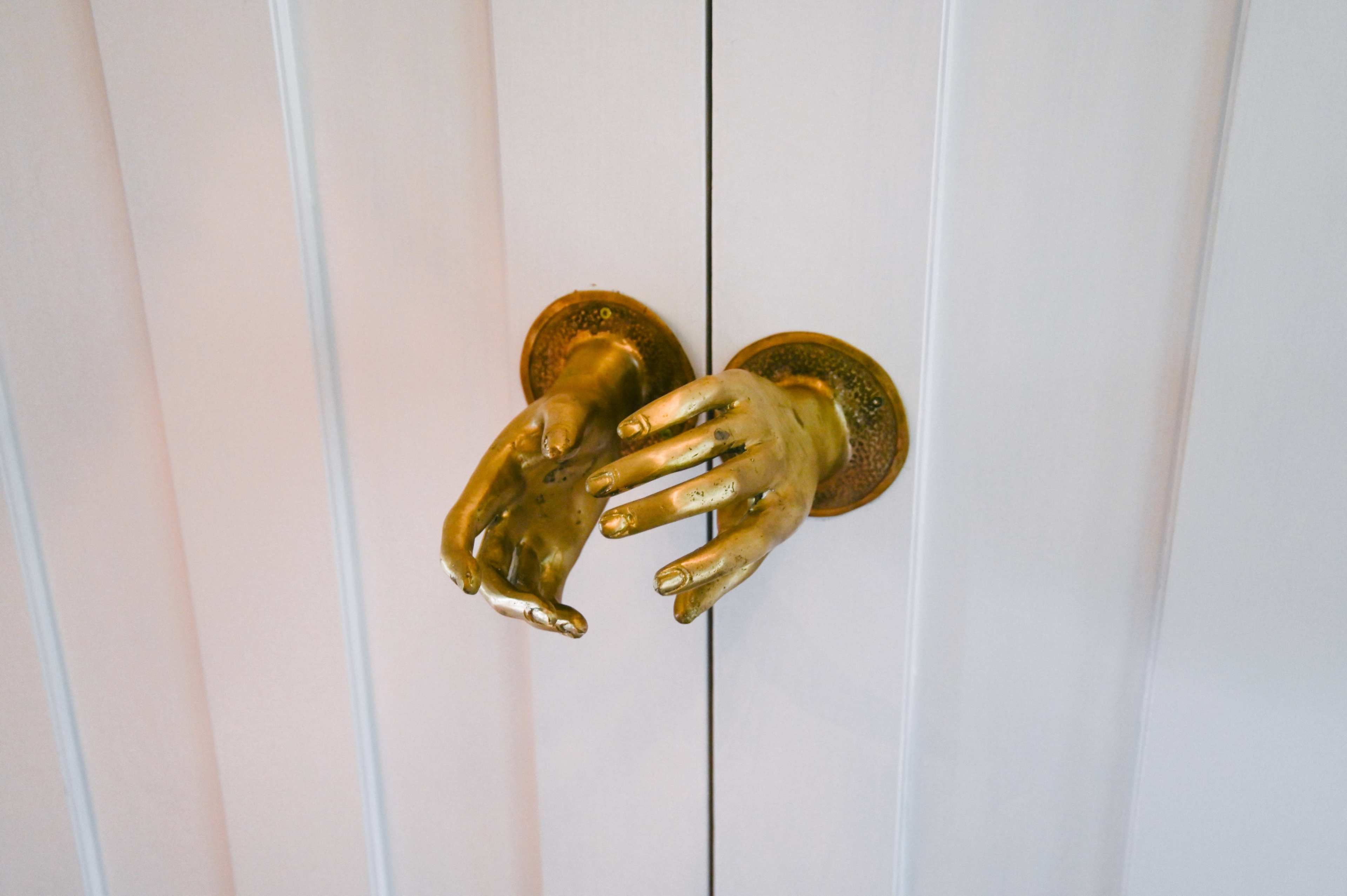 A pair of brass door handles shaped like outstretched hands, attached to a white paneled door.