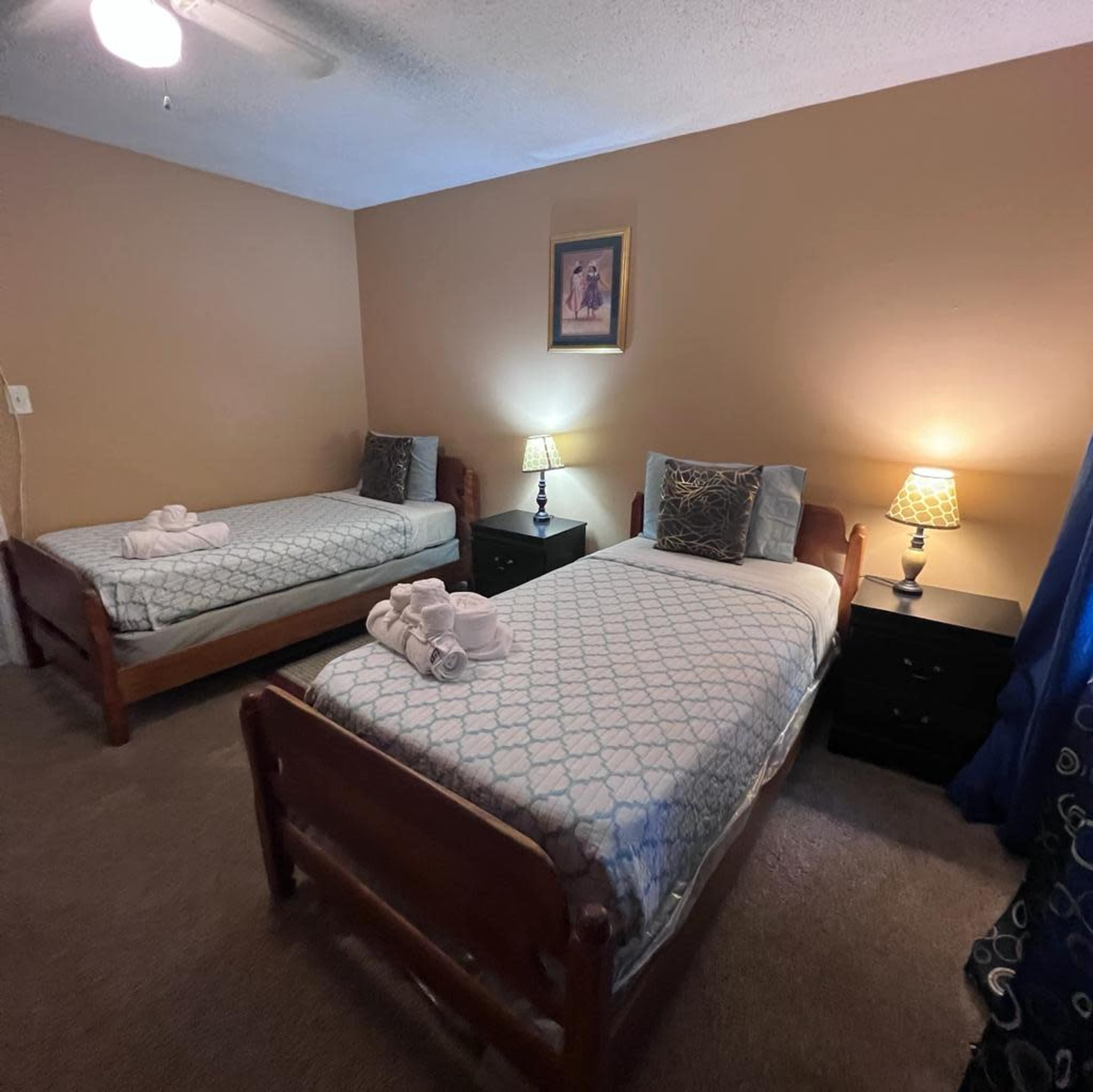 A room with two single beds, each with a patterned bedspread, side tables featuring lamps, and warm-colored walls.
