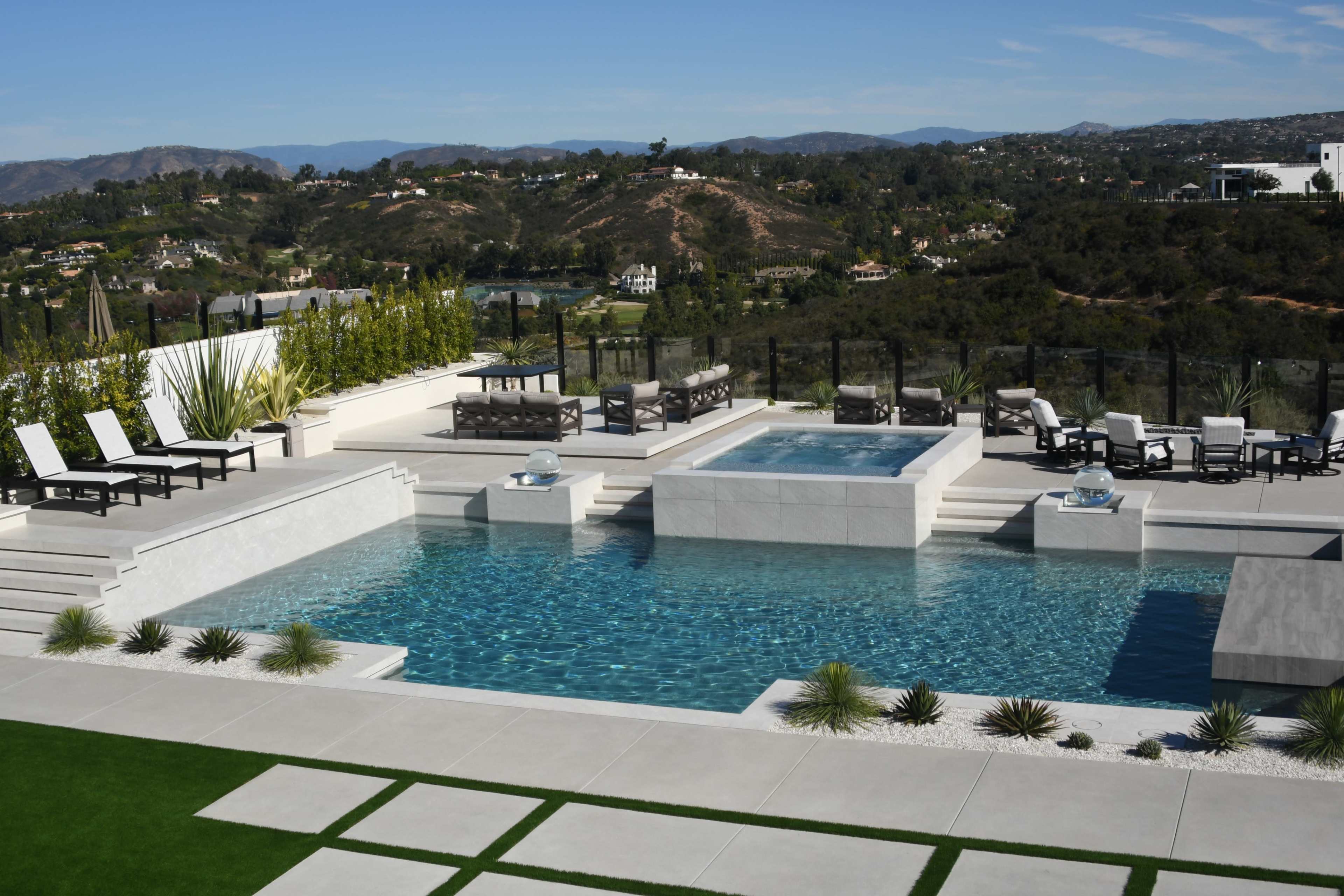 A modern outdoor space featuring a swimming pool, hot tub, and multiple seating areas overlooking a hilly landscape.