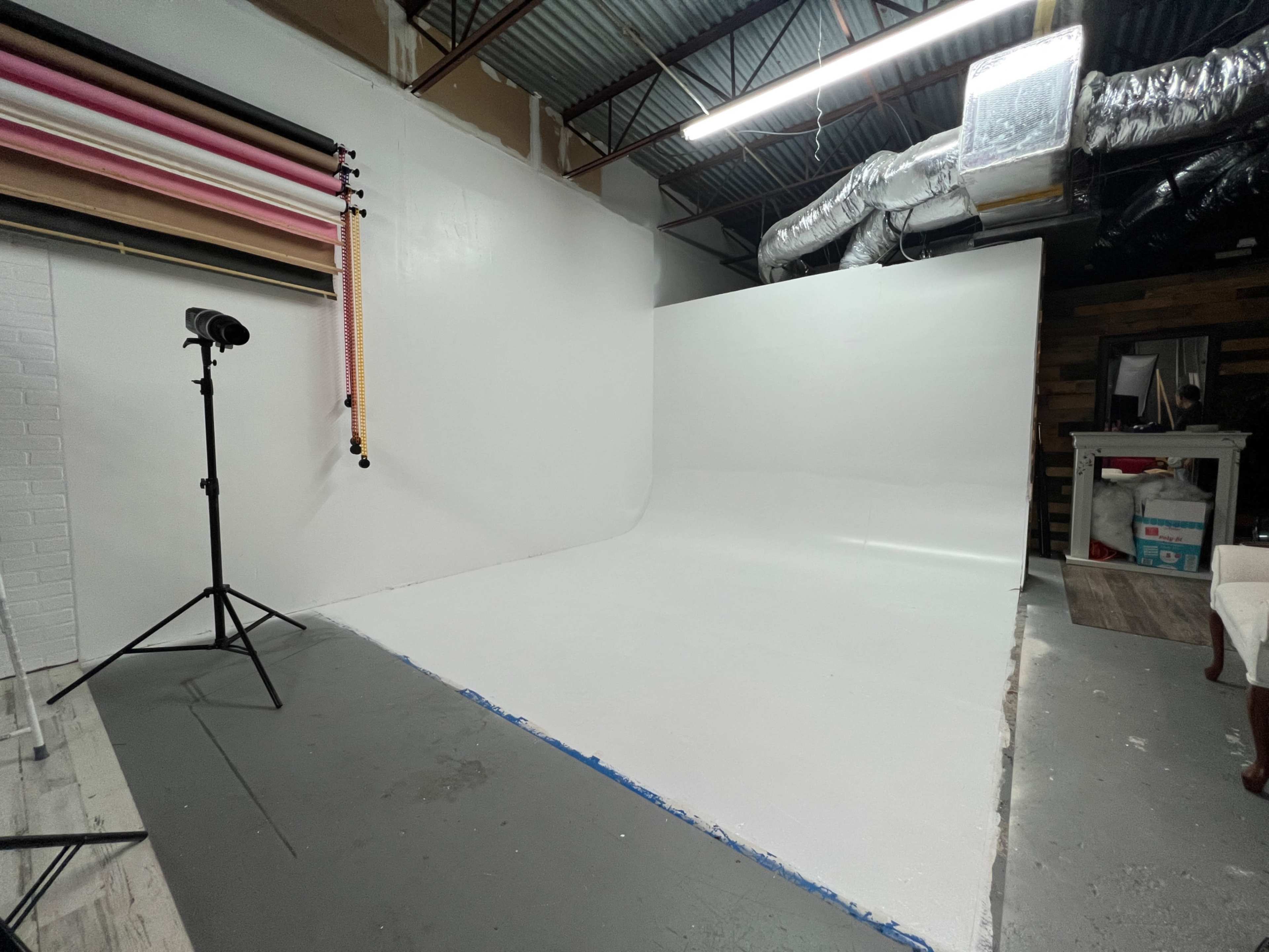 A photography studio with a seamless white backdrop, a tripod-mounted light, and colored backdrop rolls on the wall.