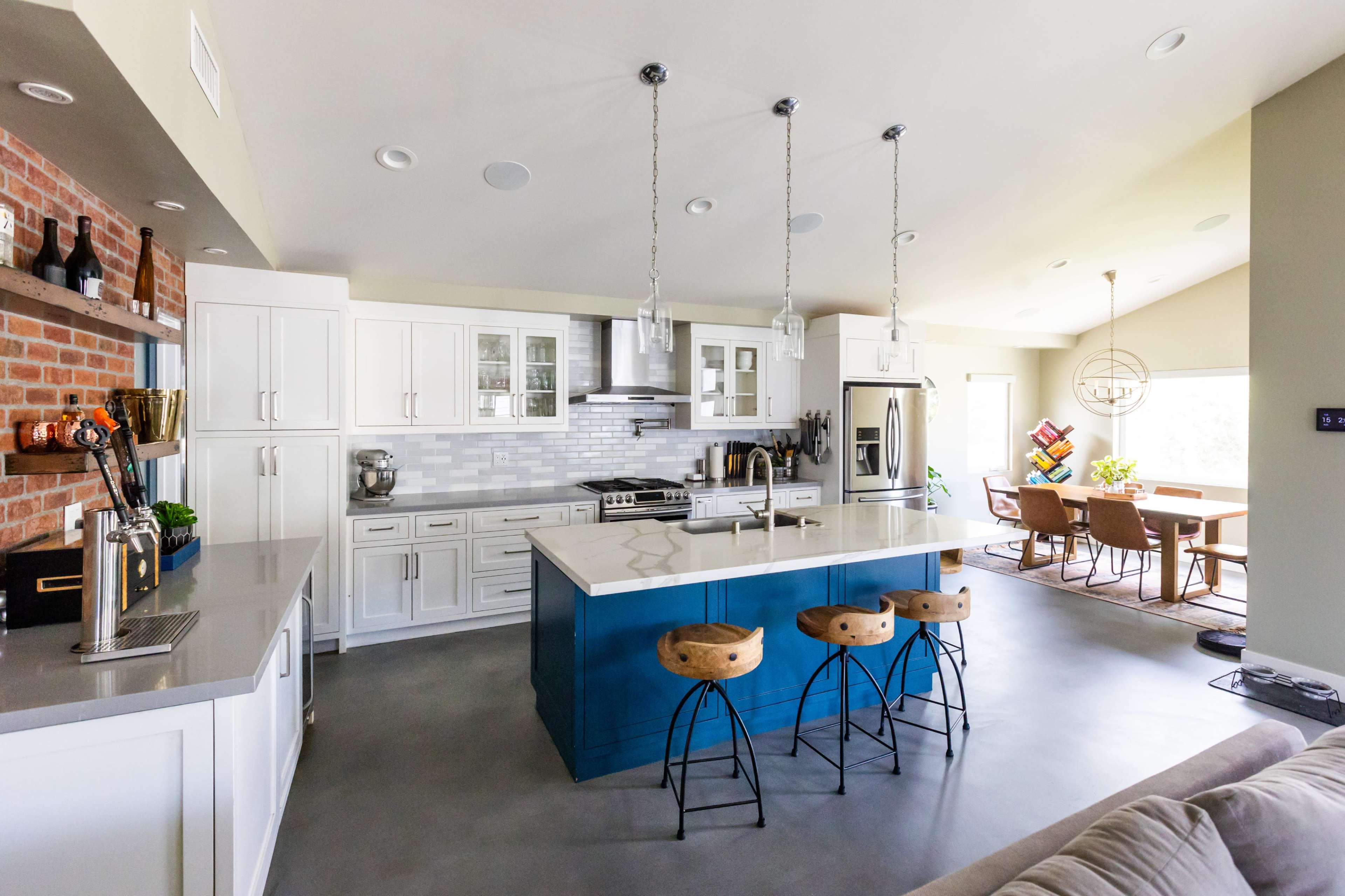 A modern kitchen with a central island featuring bar stools, white cabinetry, and a combination of brick and tiled walls.