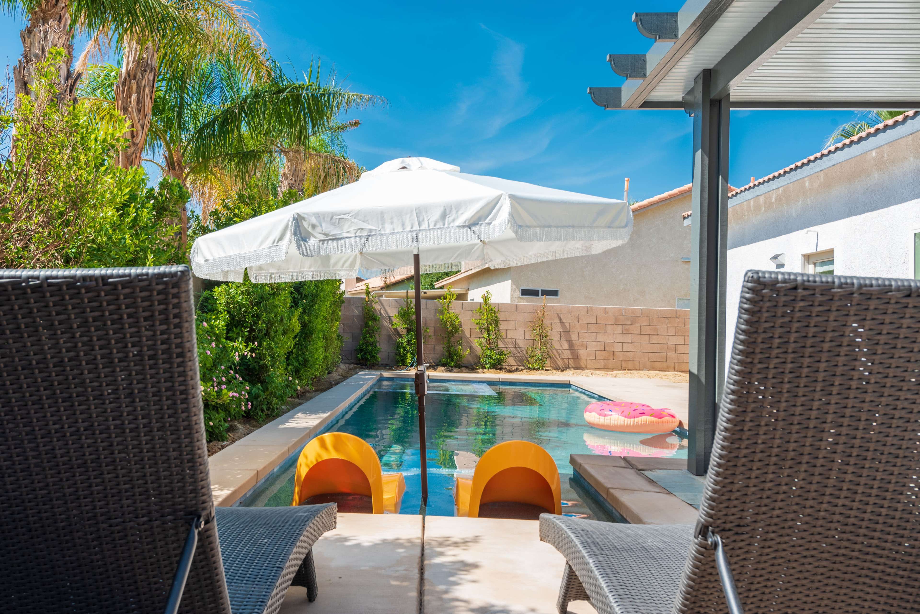 A view of a backyard pool area featuring two lounge chairs facing a swimming pool with an umbrella and two orange floatation tubes.
