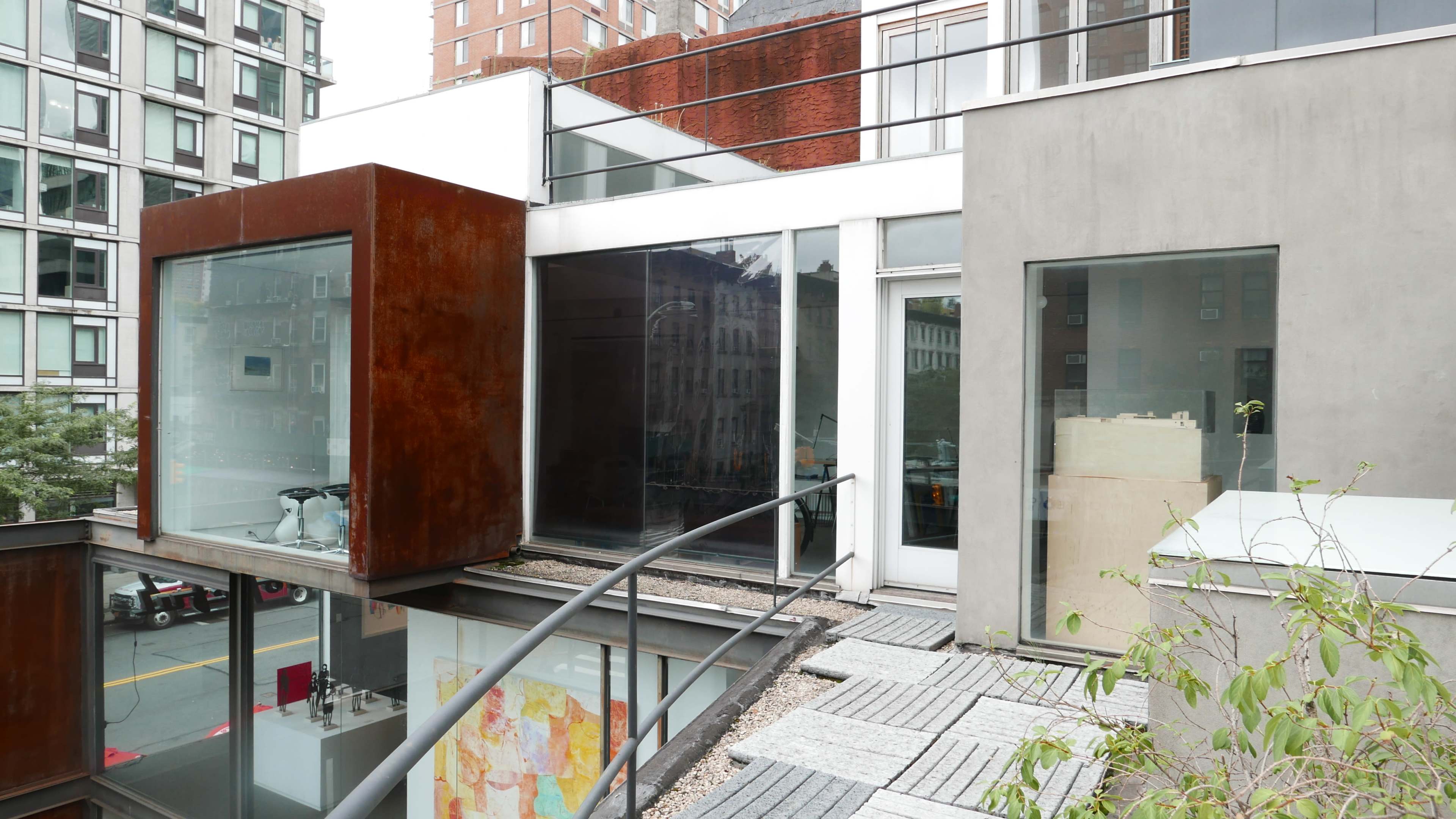A modern building featuring a combination of glass and concrete surfaces, with a metal-clad extension and a balcony overlooking a city street.
