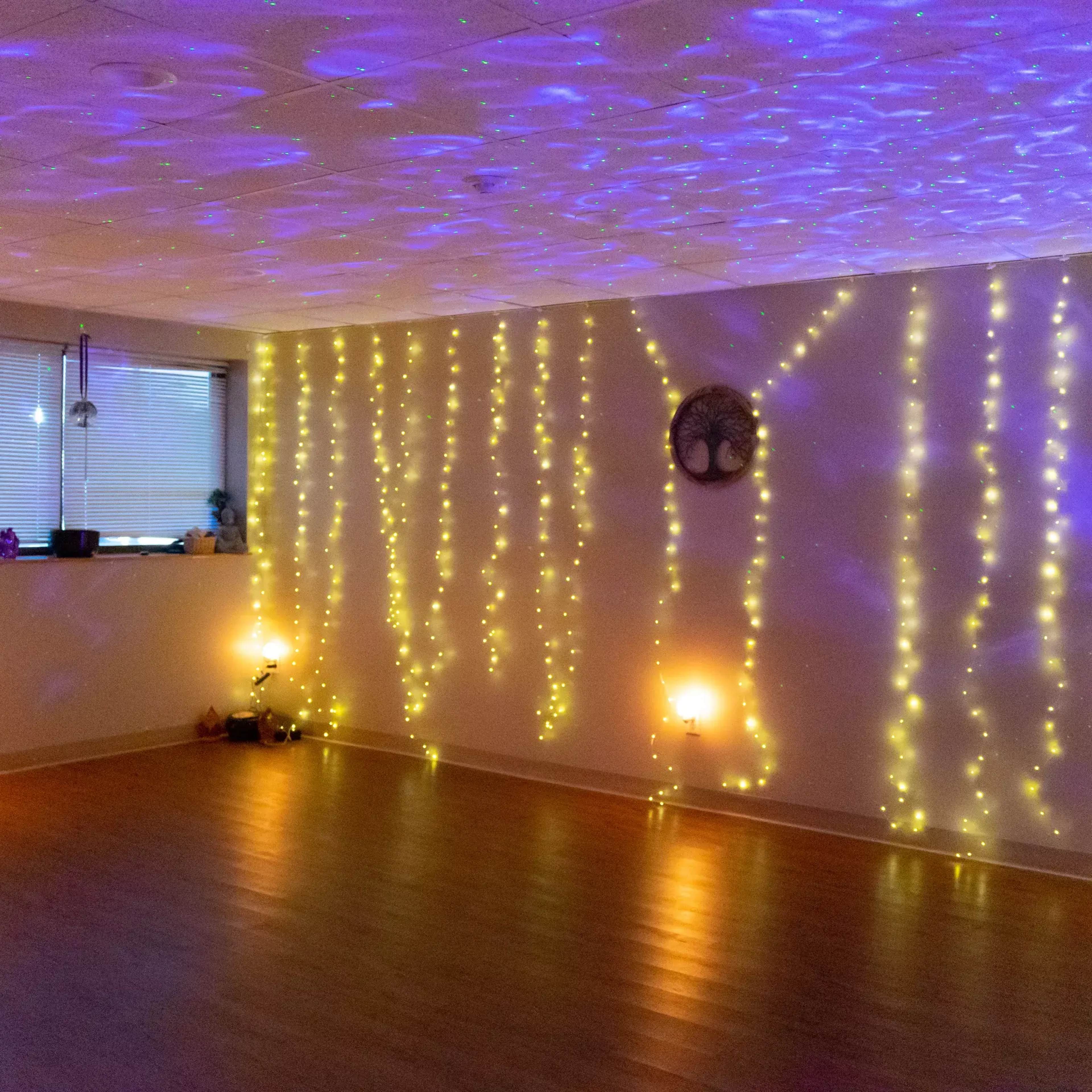 A dimly lit room with walls decorated by strings of yellow fairy lights and a soft purple light projection on the ceiling.