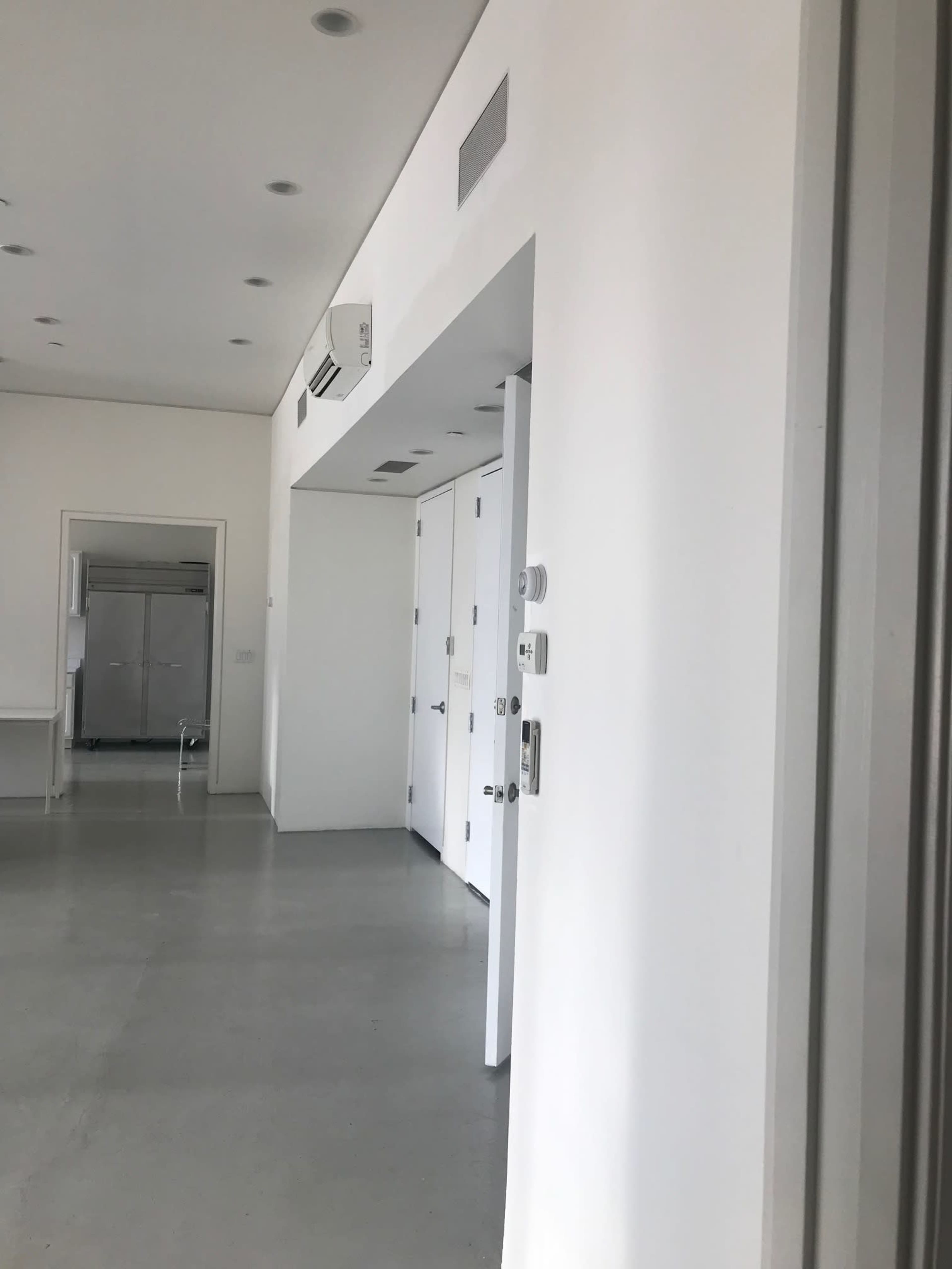 A minimalist interior space featuring white walls, a concrete floor, and a doorway leading to a different room.