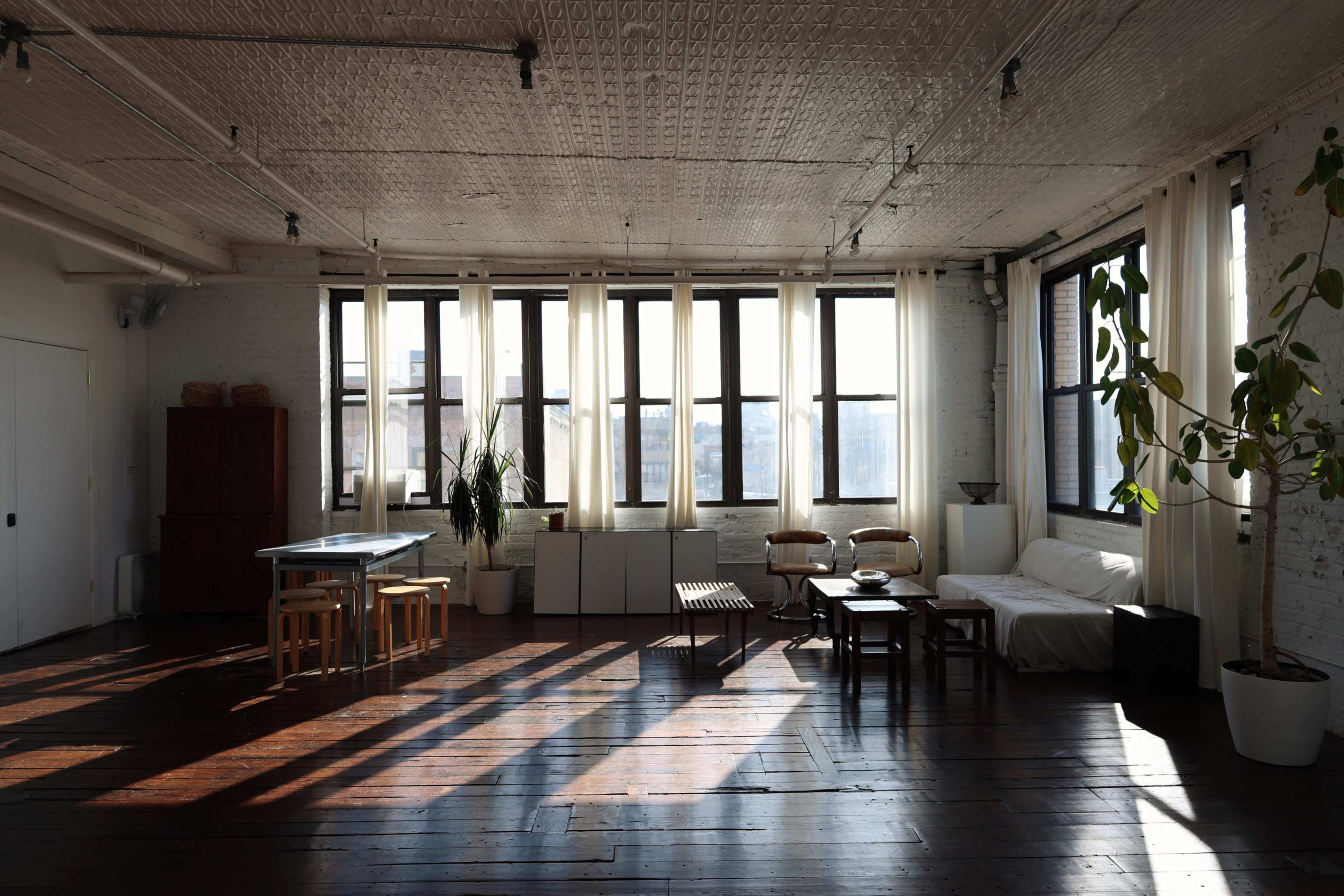 A spacious loft with large windows, wooden floors, and minimalist furniture, illuminated by natural light.
