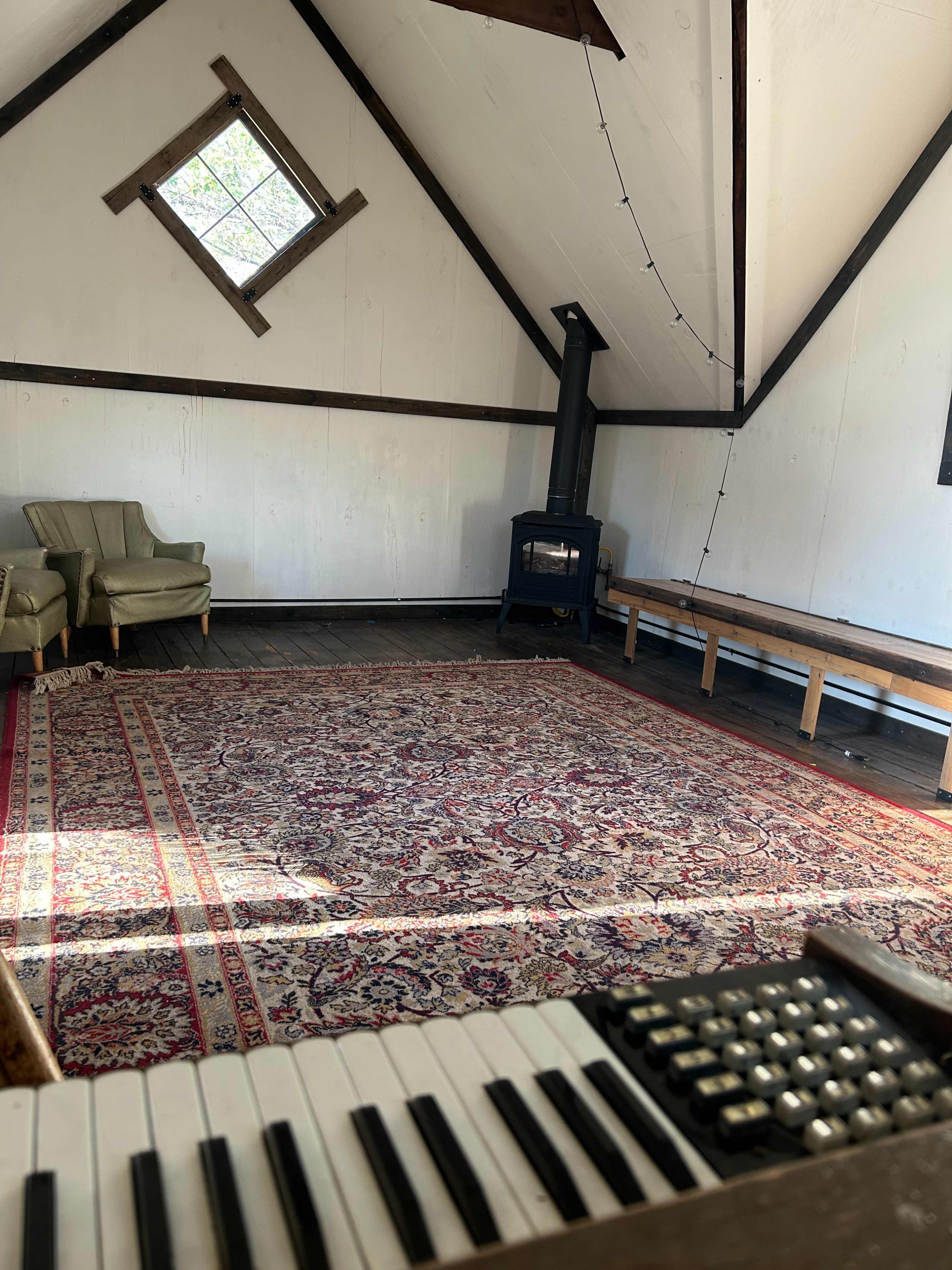 The image shows an empty room with a patterned rug, a green armchair, a wood stove, and a keyboard in the foreground.