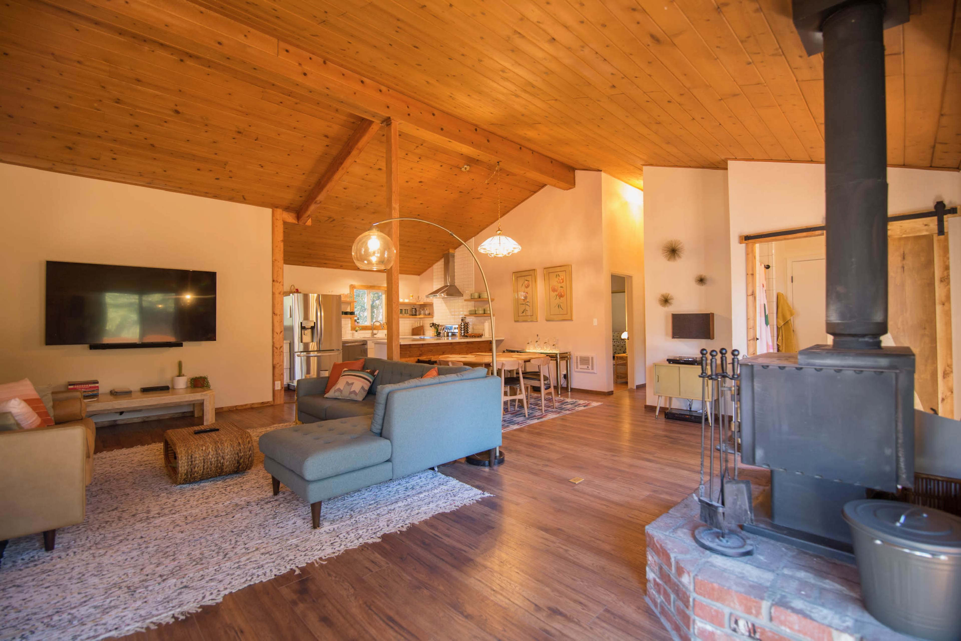 A spacious living area with a wooden ceiling, a television on the wall, and furniture arranged around a central rug.