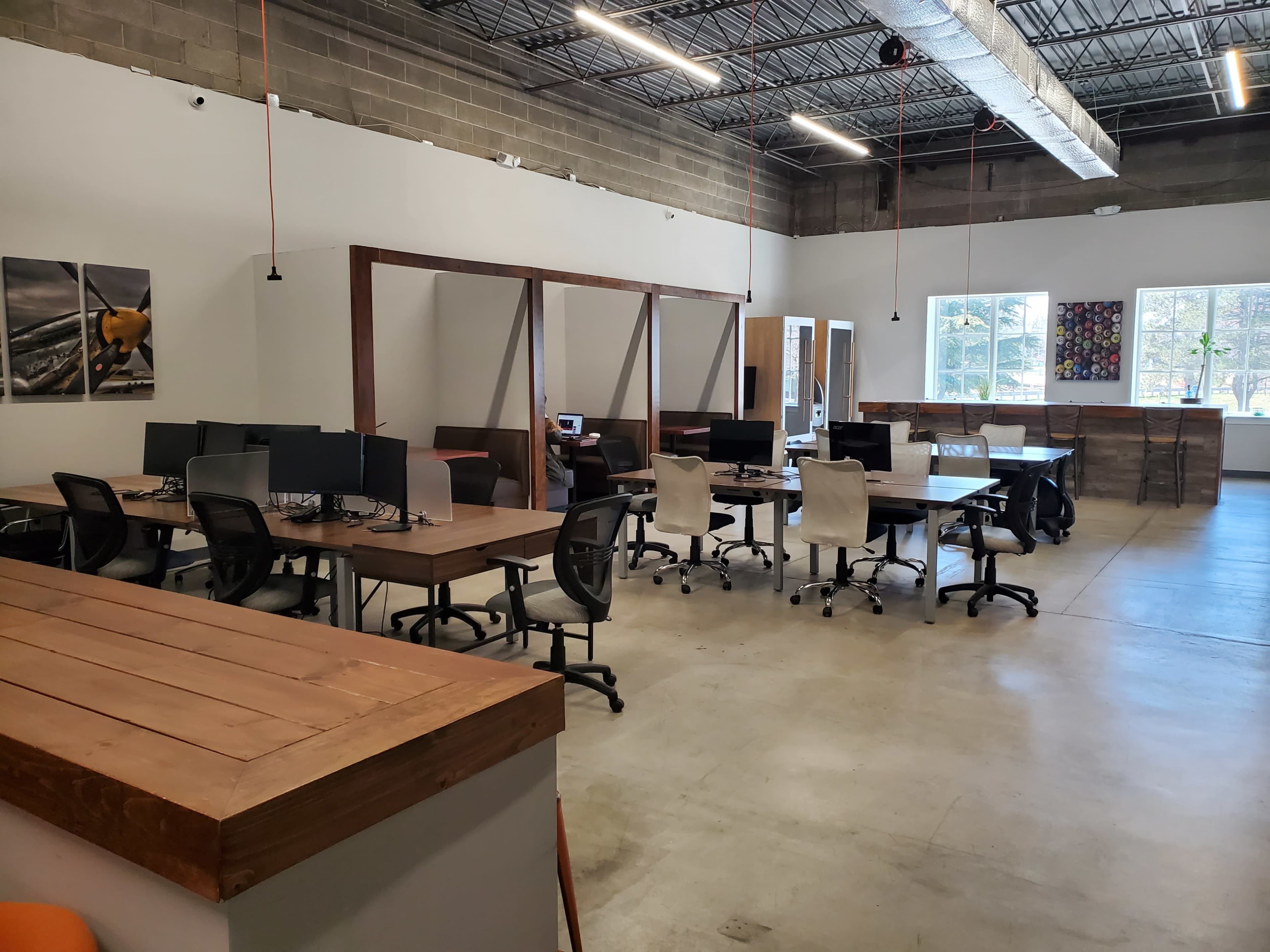 The image depicts a modern office space featuring multiple workstations with computers, wooden desks, and a bright, open layout.