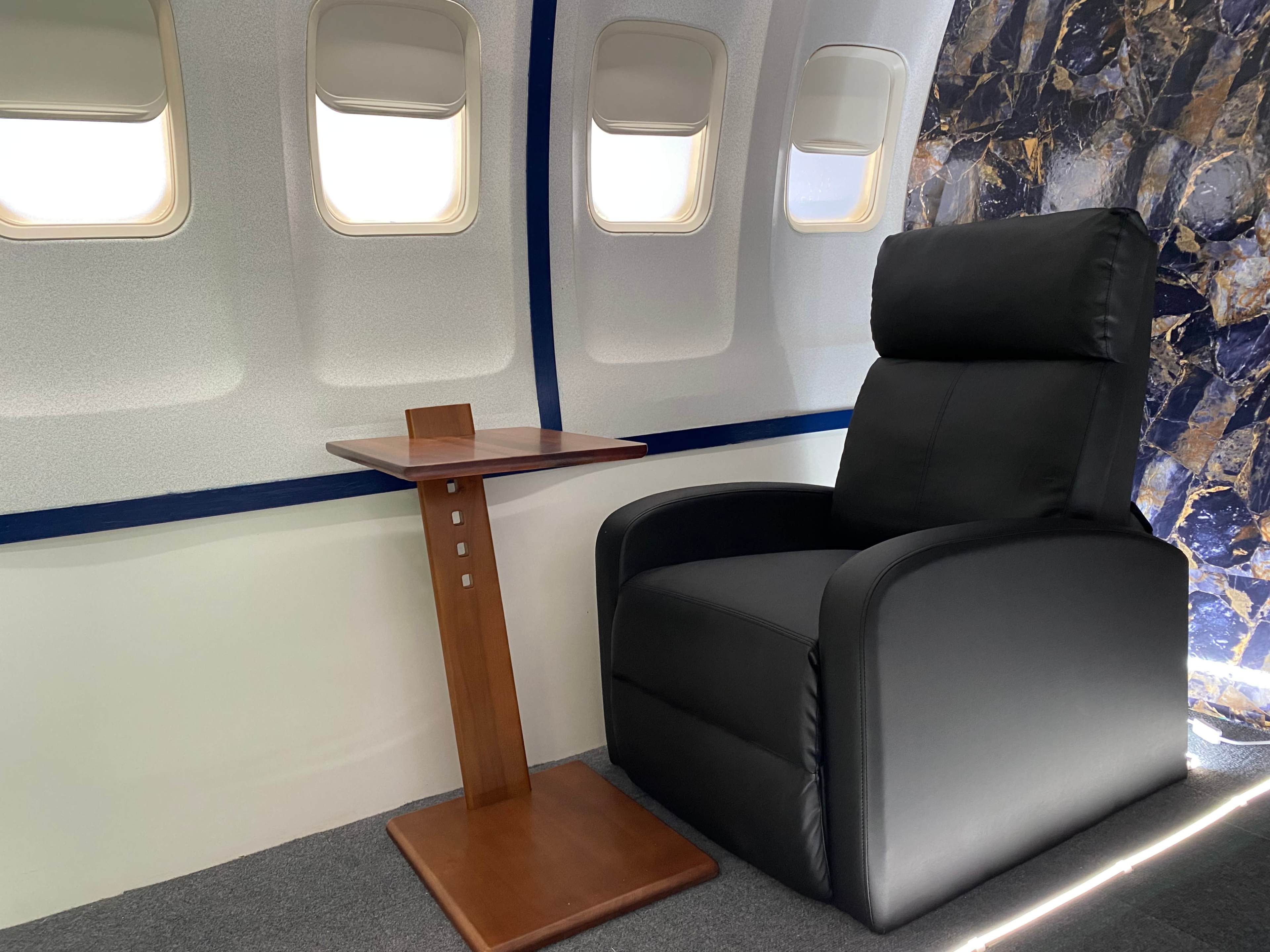 A modern black armchair beside a wooden side table in a spacious interior with large windows.