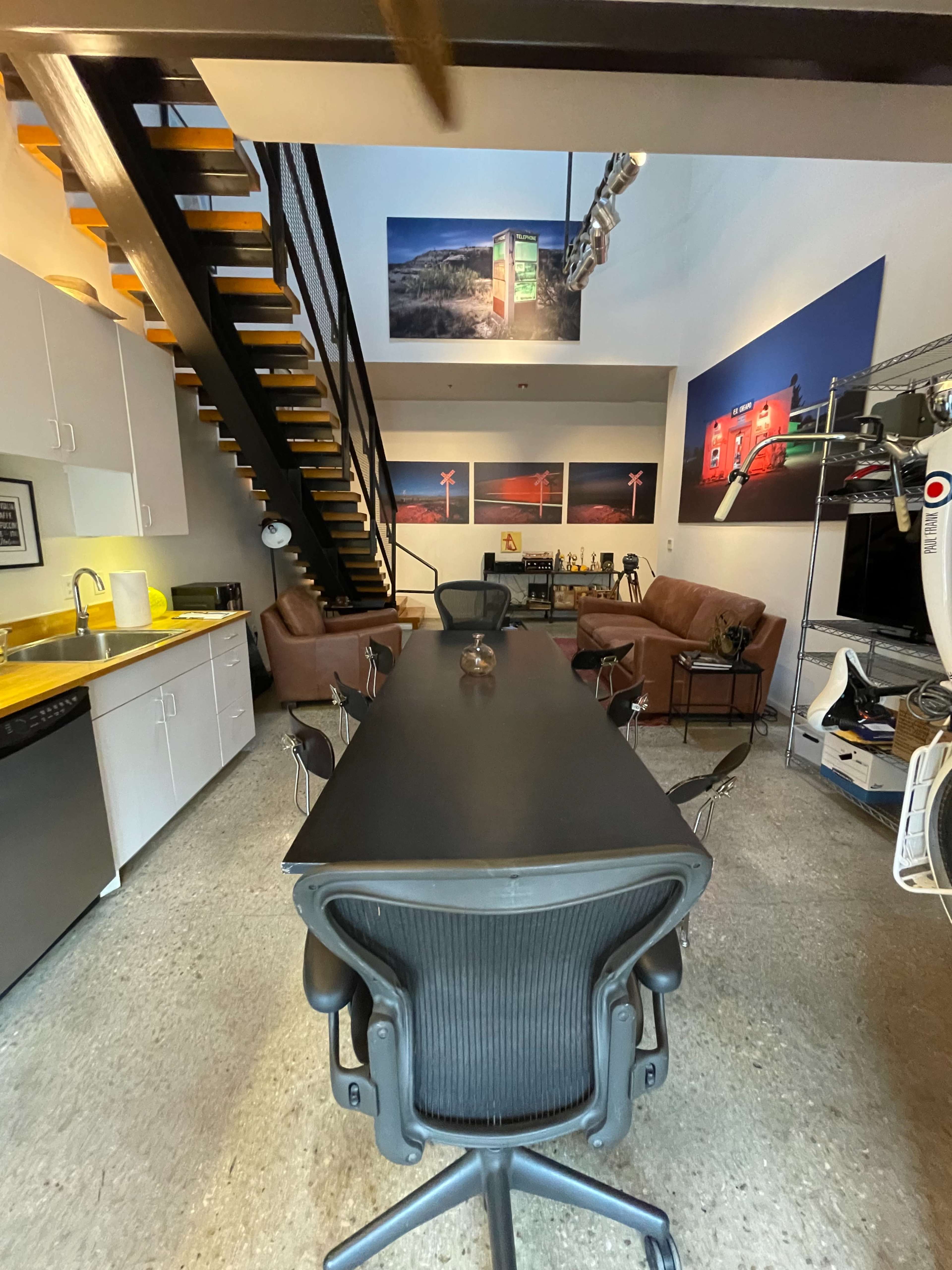 A modern office space with a long black conference table, several chairs, a staircase, and large photographs on the walls.