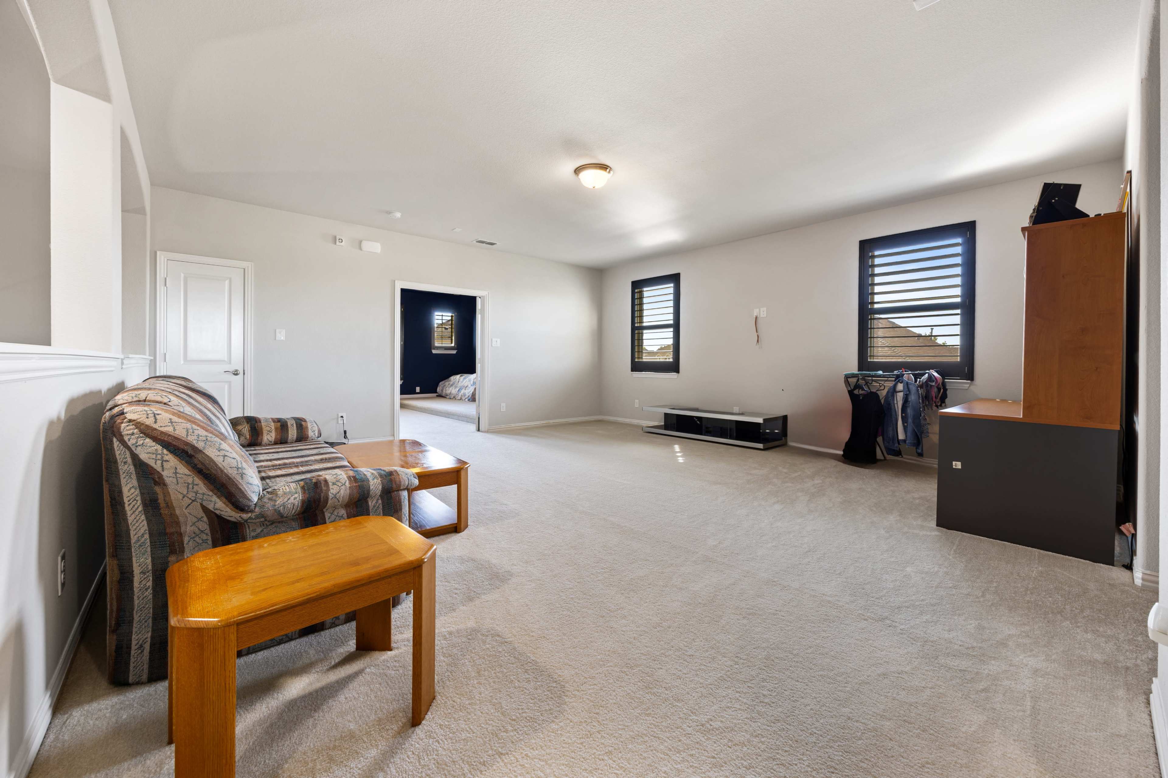 The image shows a spacious room with beige carpet, a striped couch, a small wooden table, and a media console against the wall.