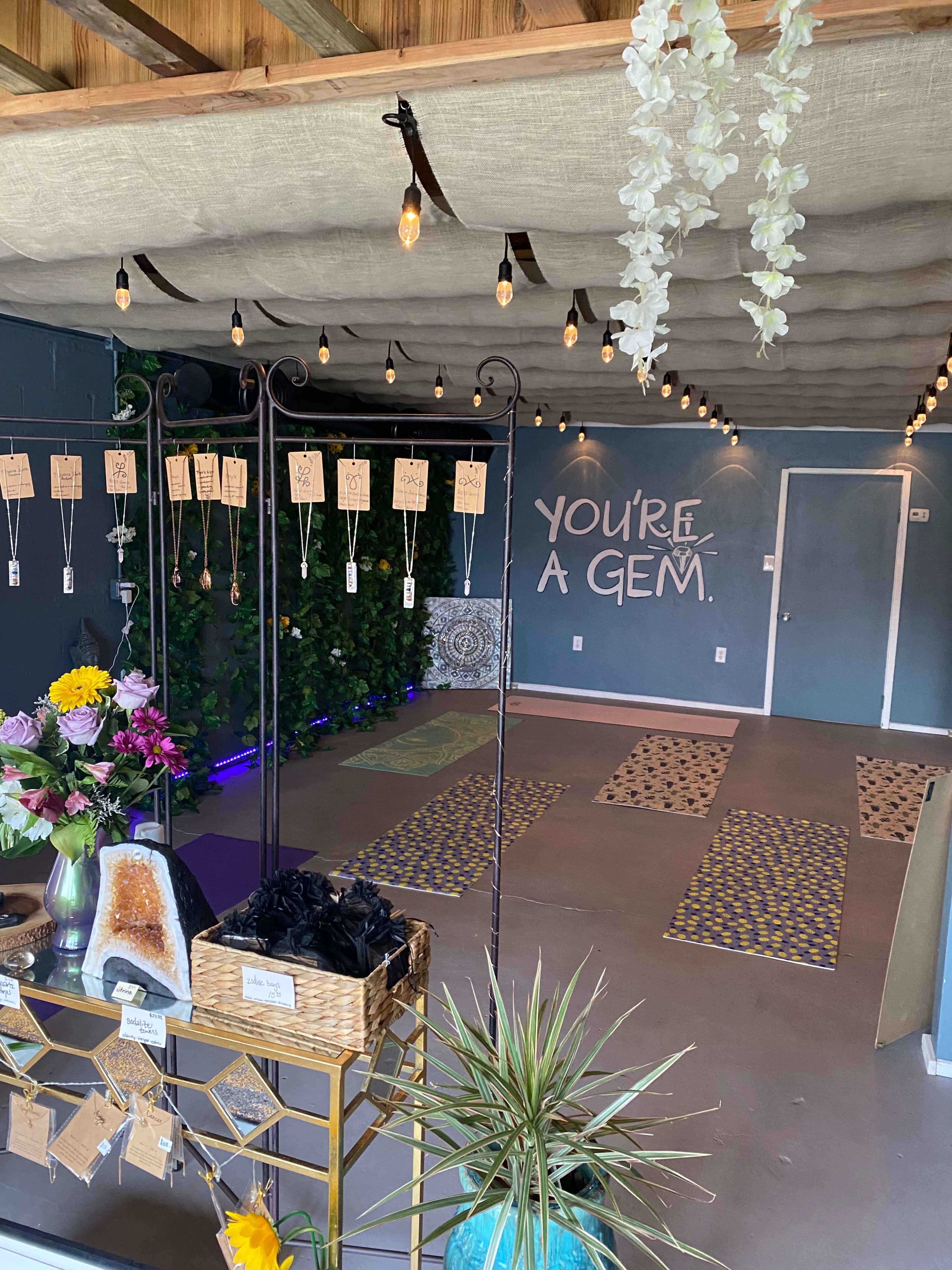 A cozy room with a decorative ceiling, string lights, a flower arrangement, gemstones for sale, and yoga mats arranged on the floor.
