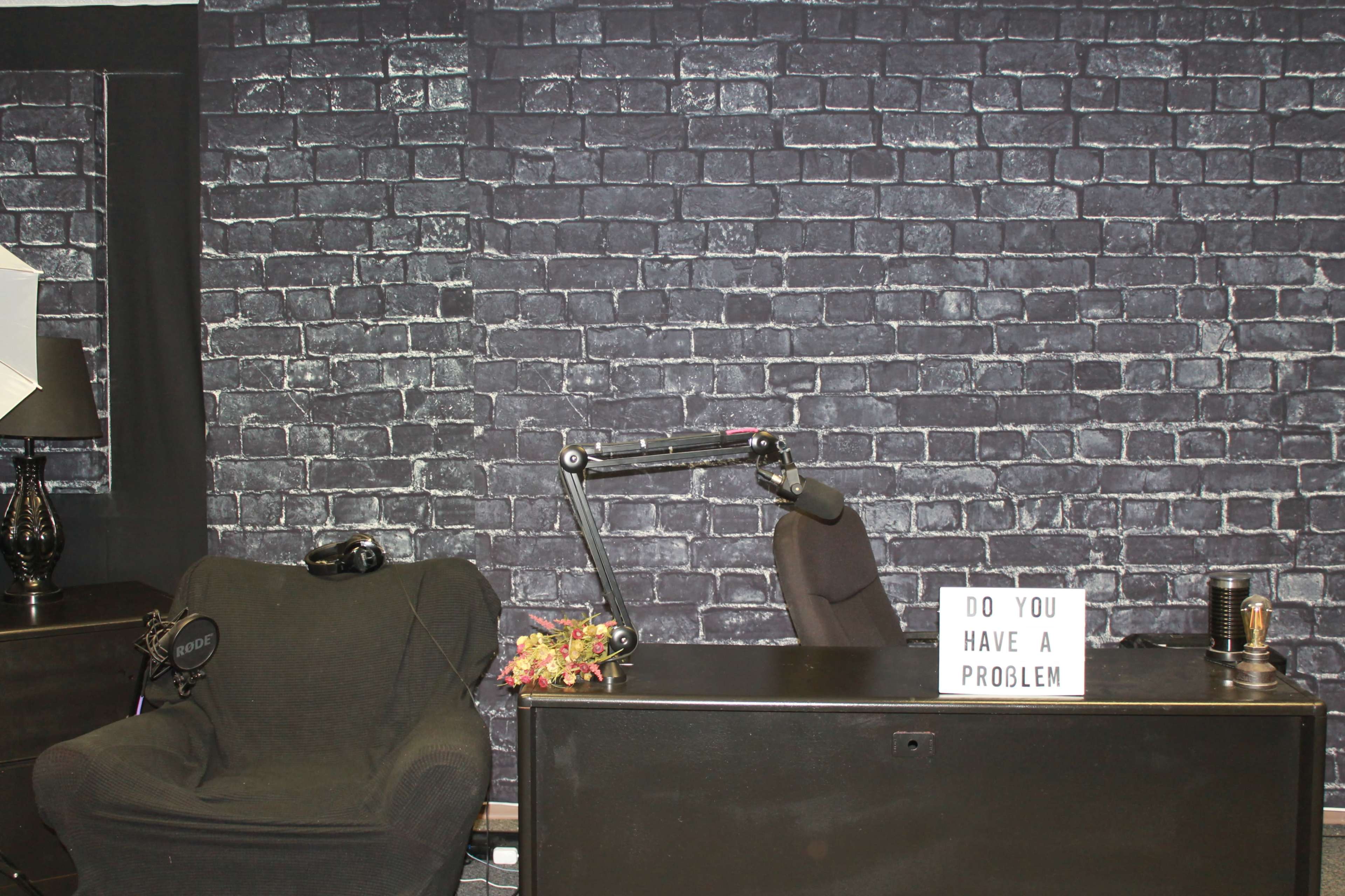 A modern office space with a black brick wall, a black desk, a chair, and a sign that reads "DO YOU HAVE A PROBLEM?"