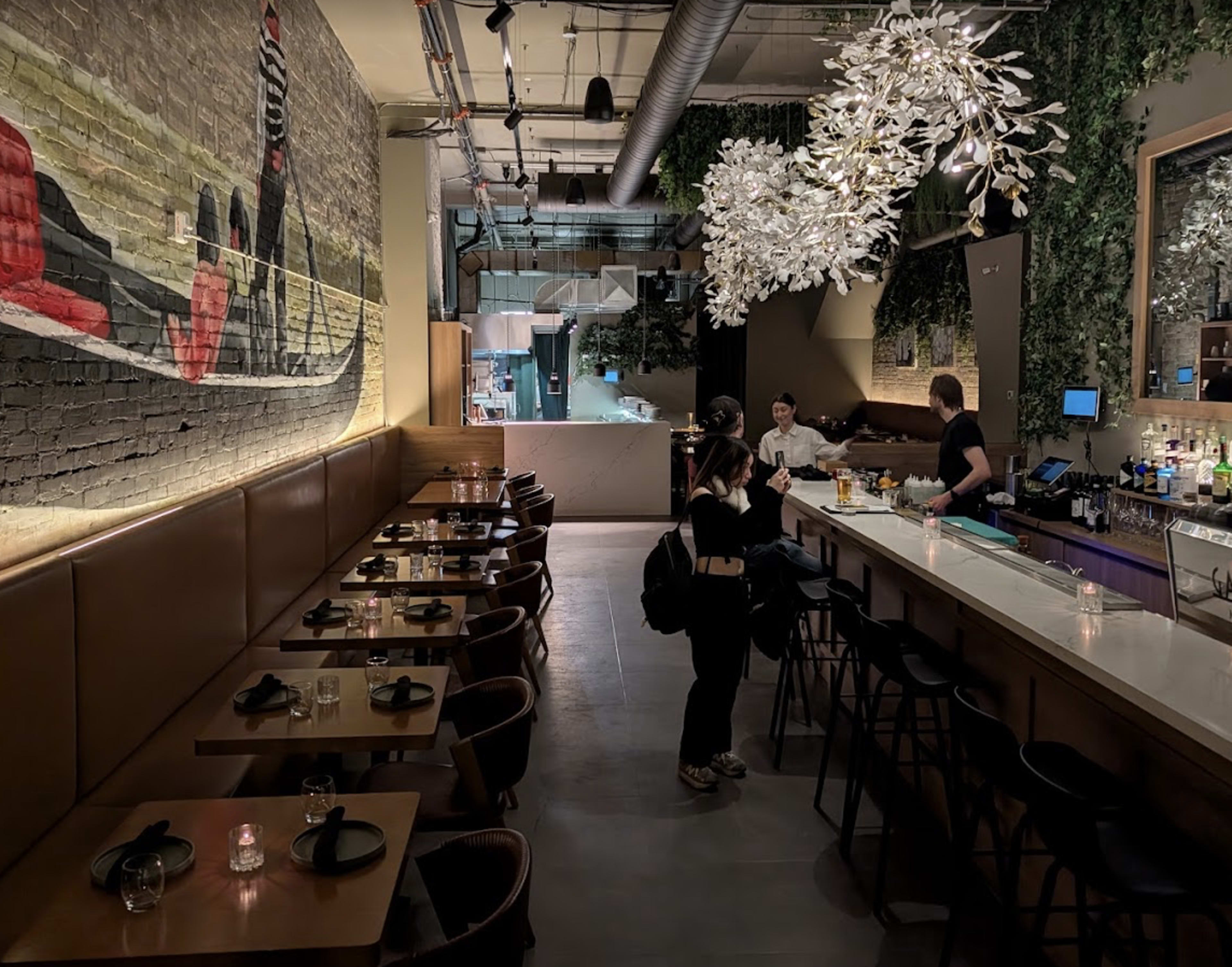 The image shows a modern restaurant interior with a bar, seating area, and decorative wall art.