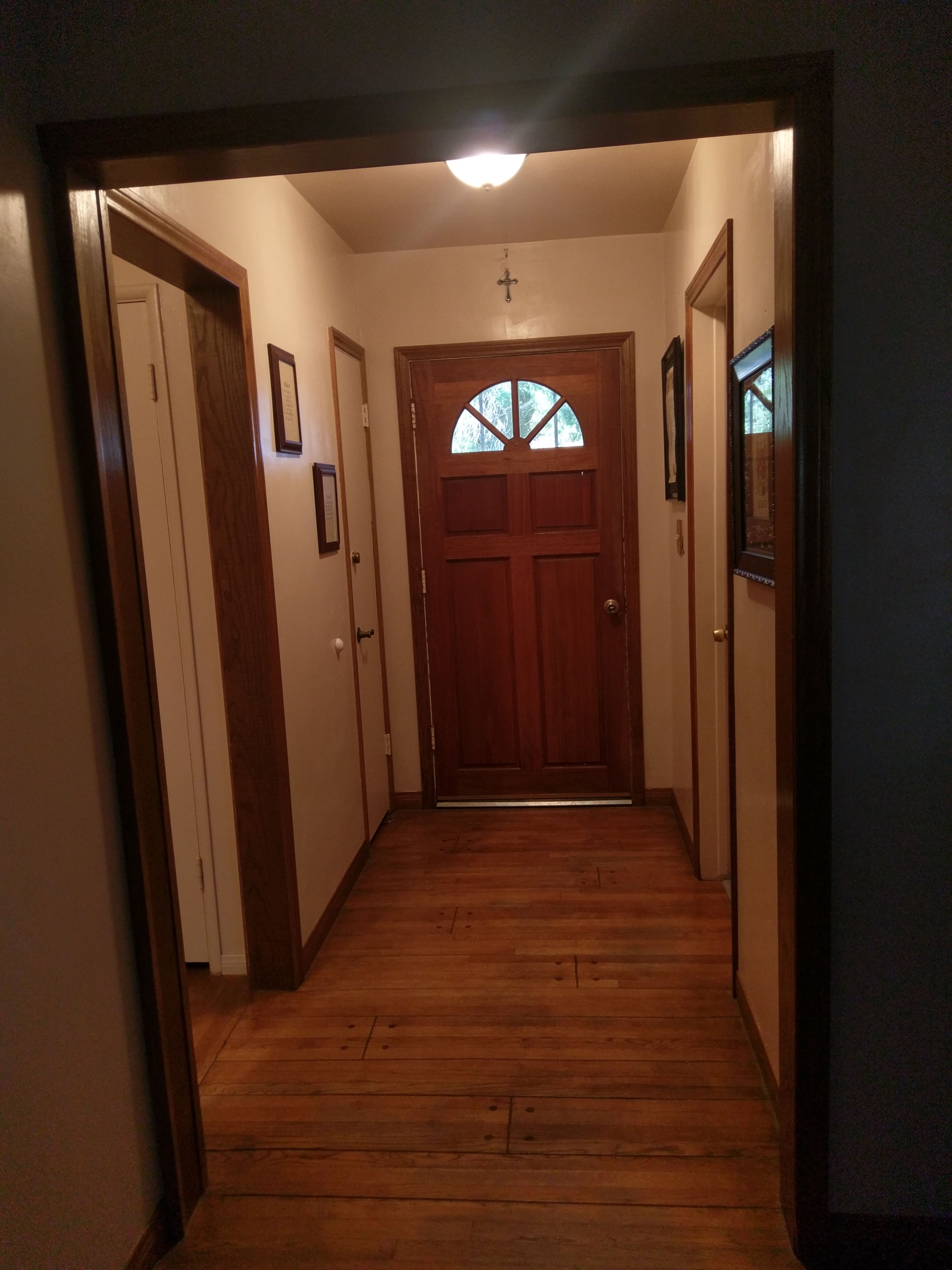 A wooden-floored hallway leading to a wooden front door with four windows above it, flanked by two side doors and framed by light-colored walls.