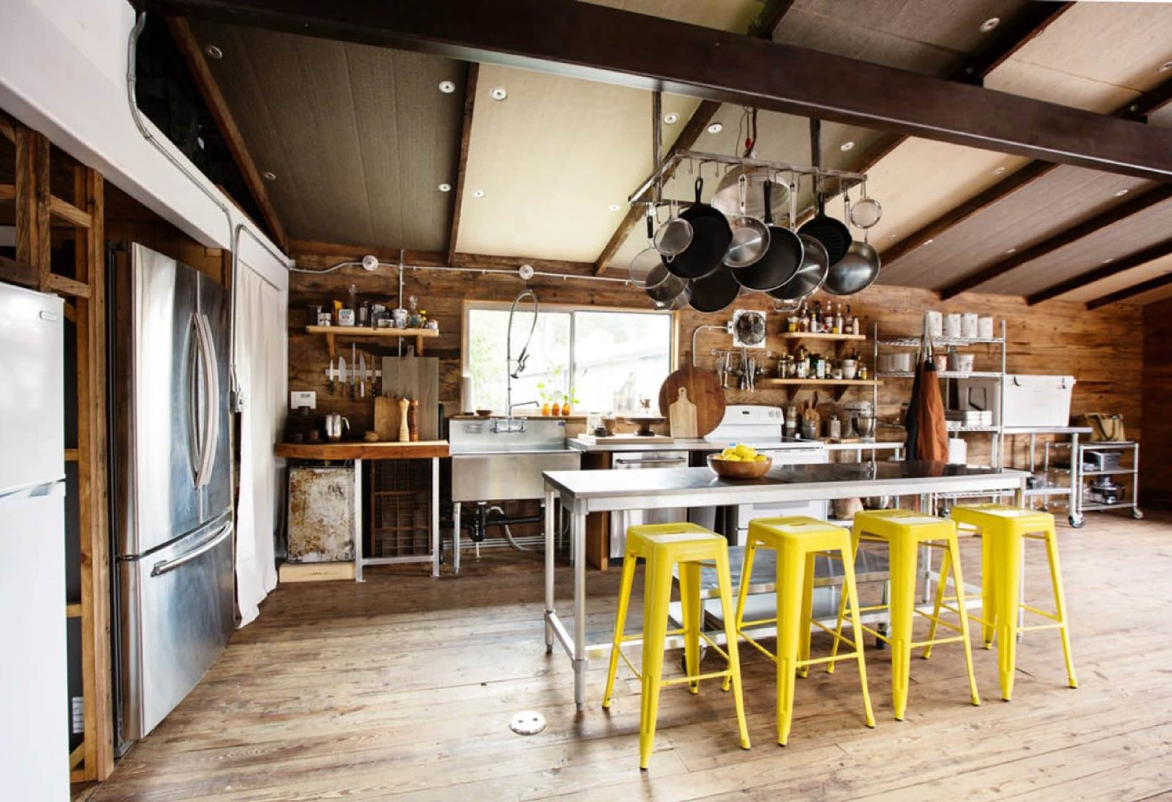 A modern kitchen features stainless steel appliances, wooden cabinetry, and yellow bar stools around a central island.