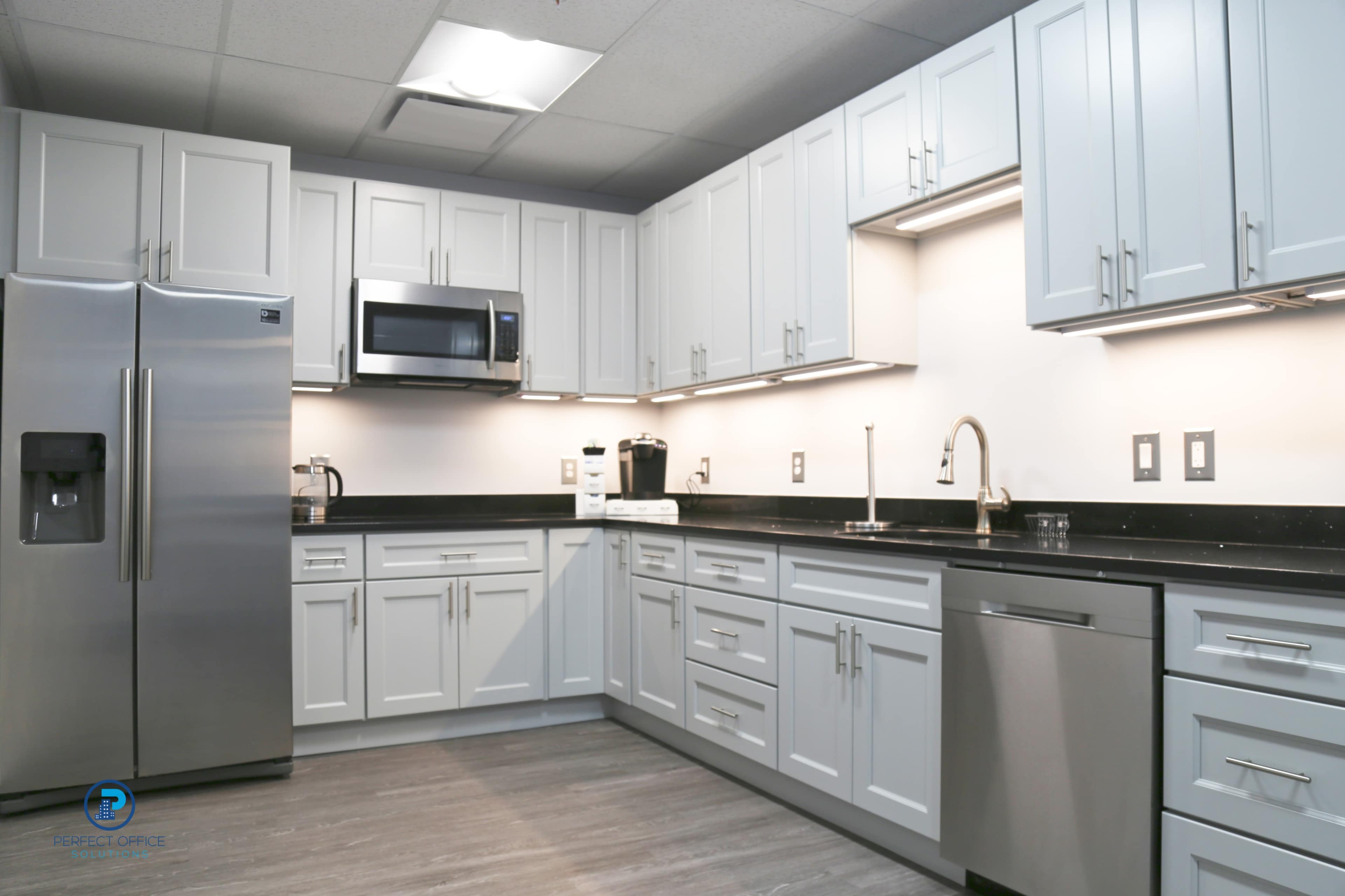The image shows a modern kitchen with light gray cabinetry, stainless steel appliances, and black countertops.