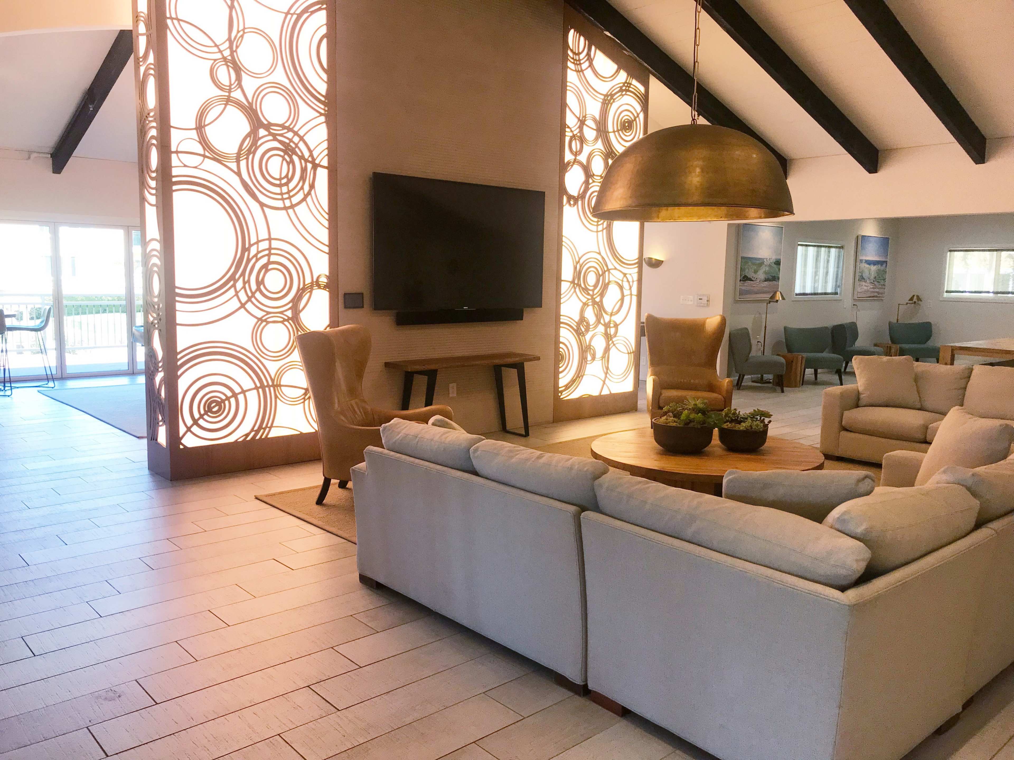 A spacious living area with a large circular table, a comfortable seating arrangement, a wall-mounted television, and a decorative backdrop featuring circular patterns.