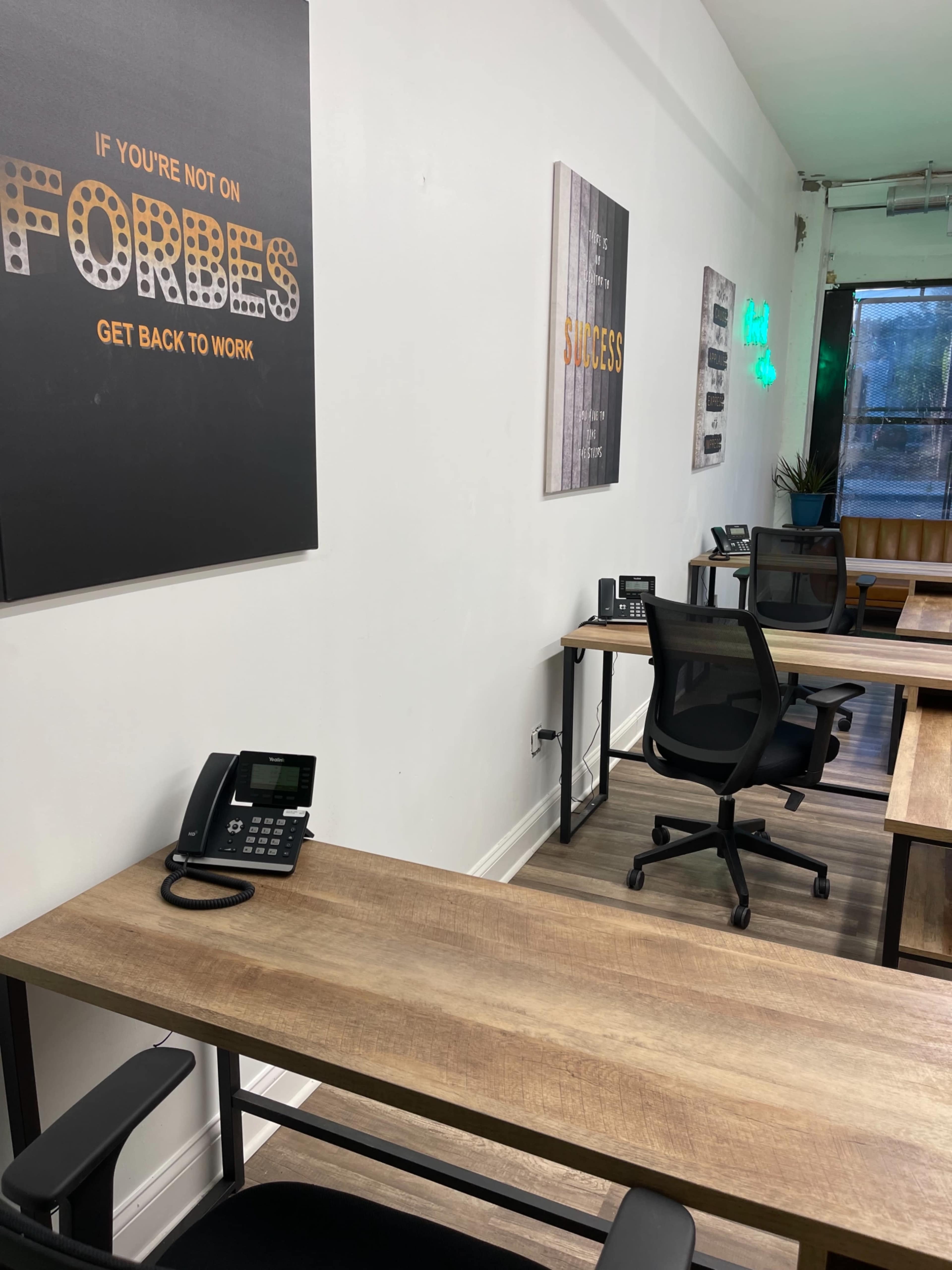 A modern office space with wooden desks, office phones, and motivational posters on the walls.